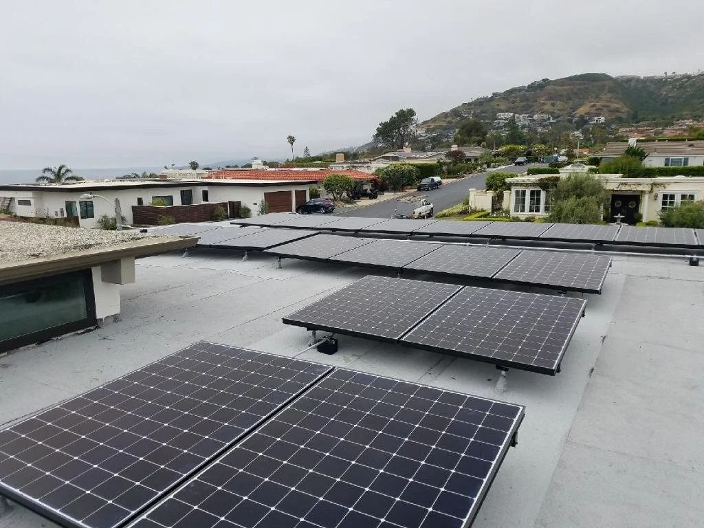 Solar panels on a rooftop overlooking a coastal neighborhood and hillside under an overcast sky