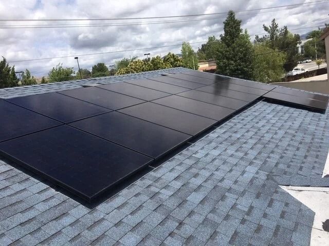 Solar panels installed on a shingled roof under a cloudy sky