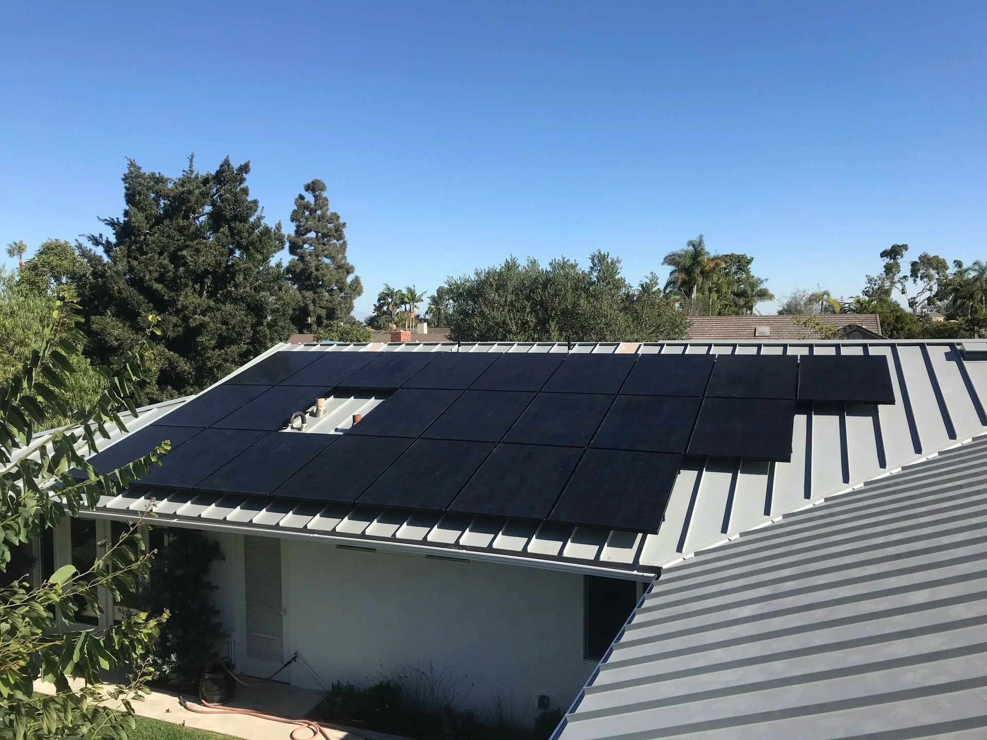 Rooftop with solar panels and a skylight under a clear blue sky, surrounded by trees