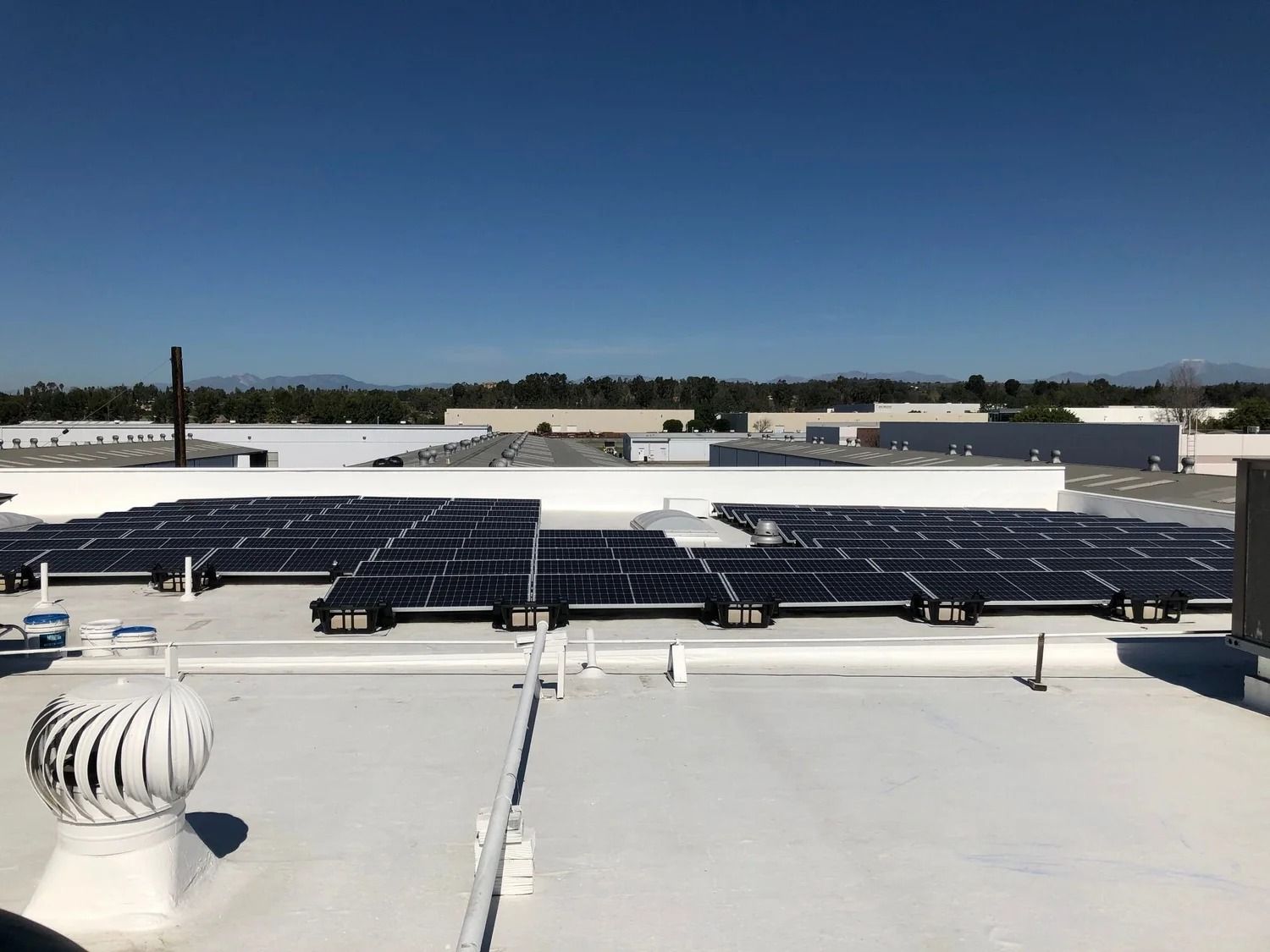 Rooftop solar panels beneath a clear blue sky, with white vents in the foreground.