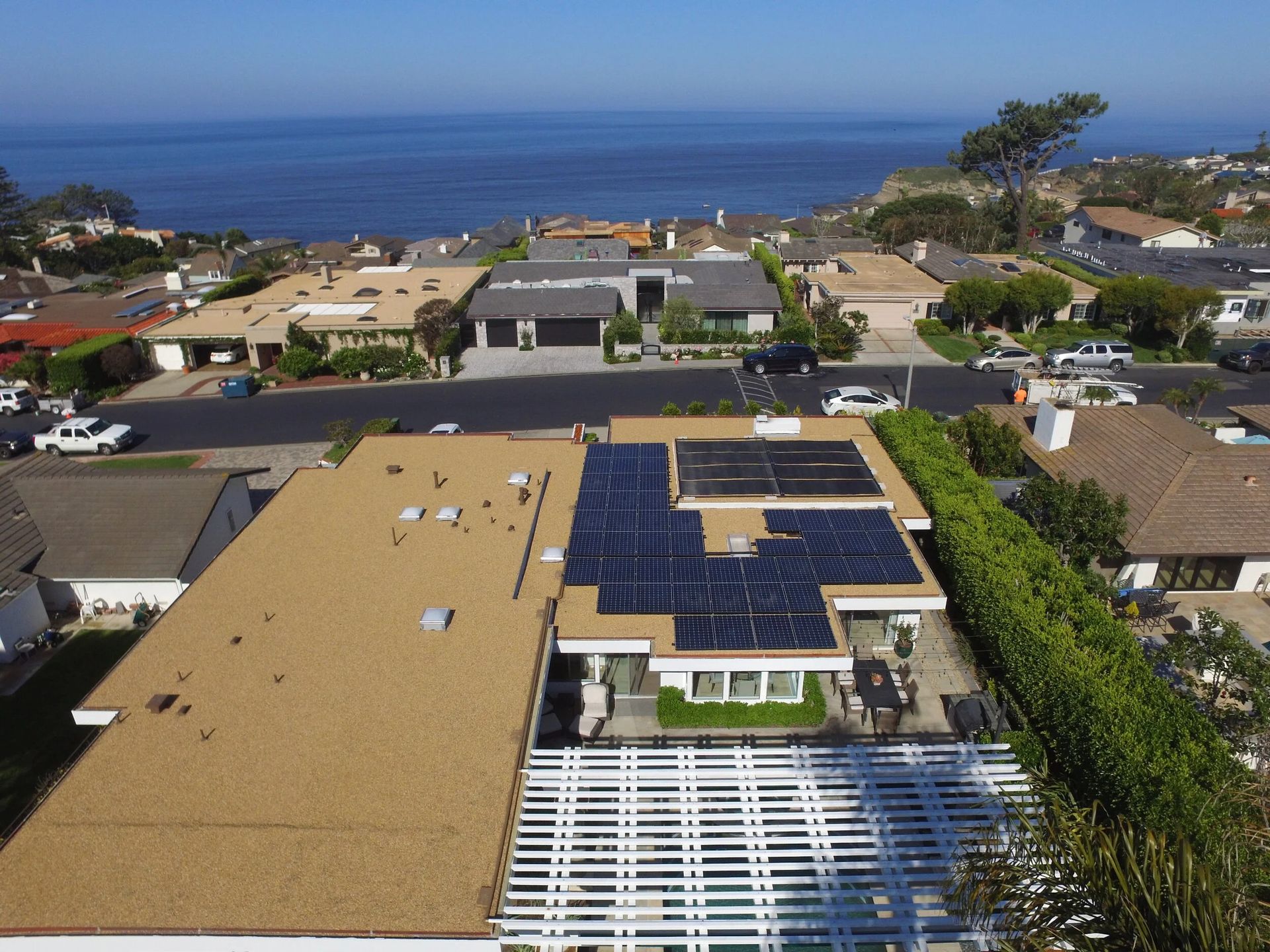 Aerial view of suburban homes near the coast, with solar panels and the ocean in the background.