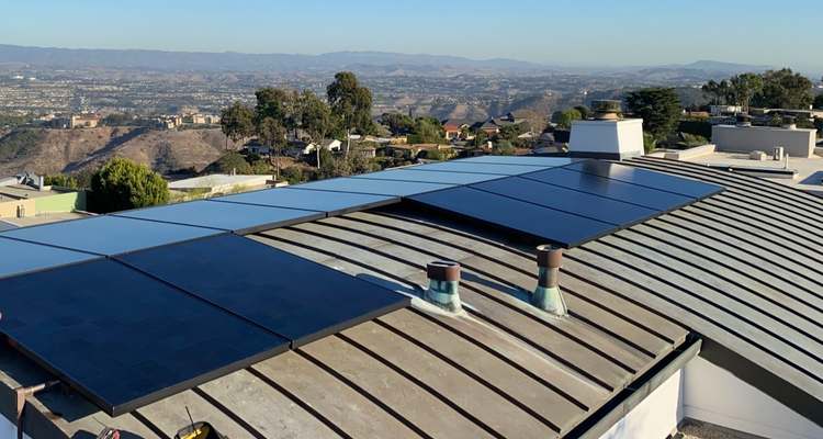 Solar panels on a rooftop overlooking a city and hills under a clear sky