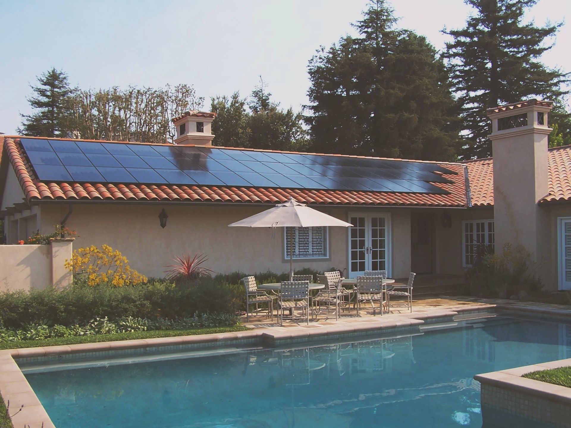 House with solar panels beside a swimming pool in a sunny backyard