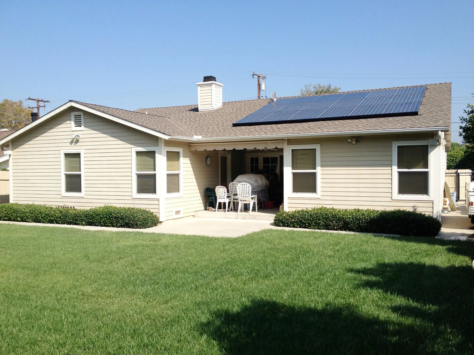 Single-story beige house with blue roof and green lawn, with chairs on the front patio