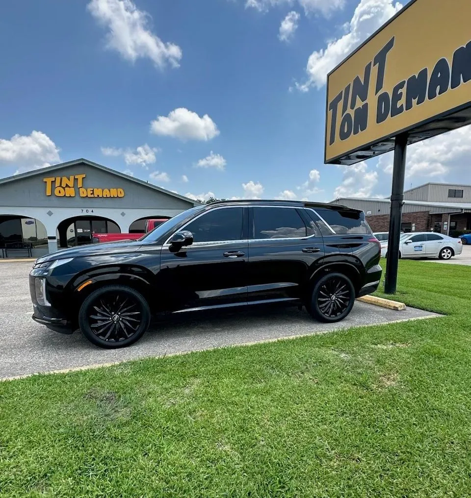 A black suv is parked in front of a tint on demand sign.