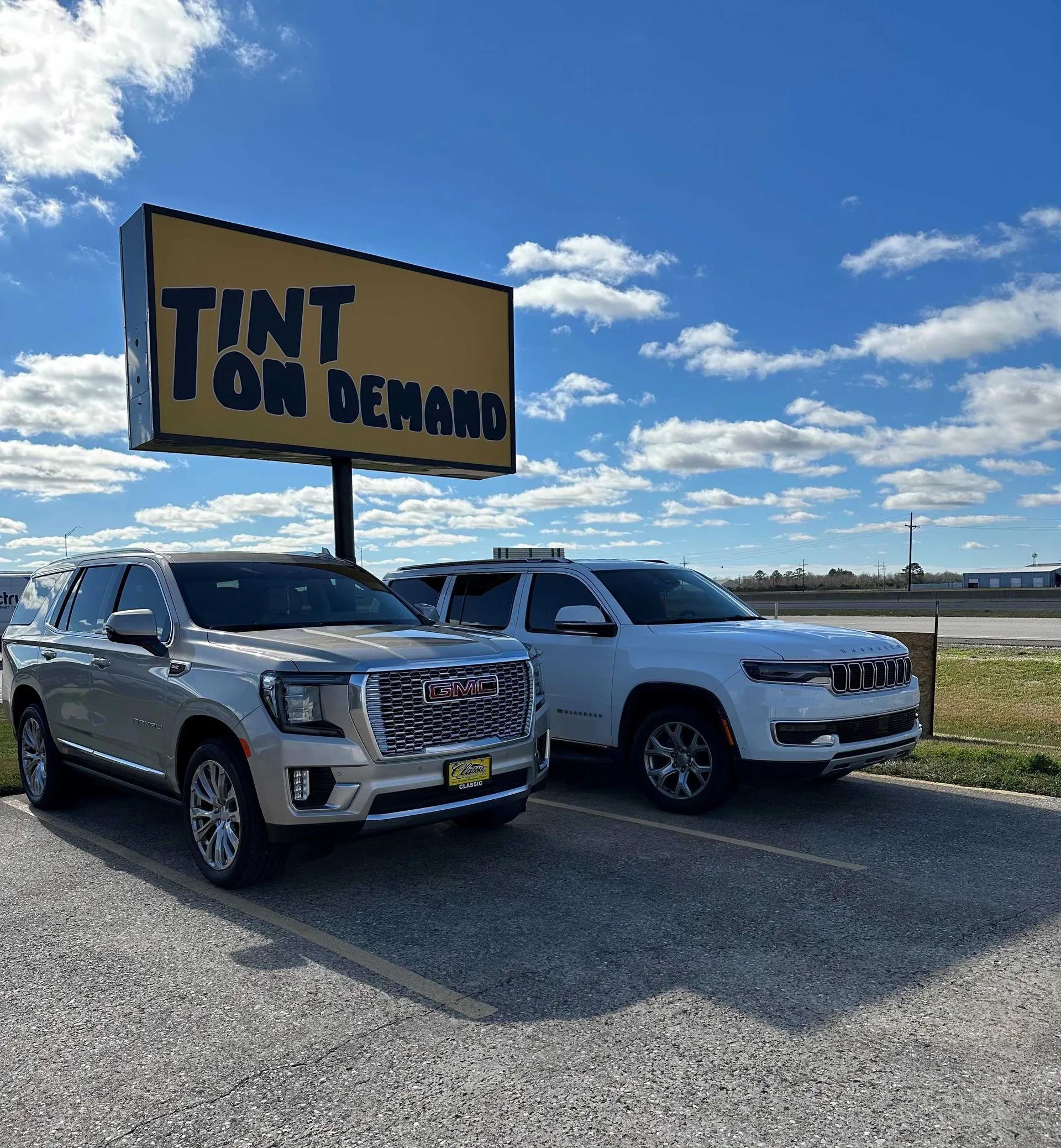 Two cars are parked in front of a tint on demand sign.