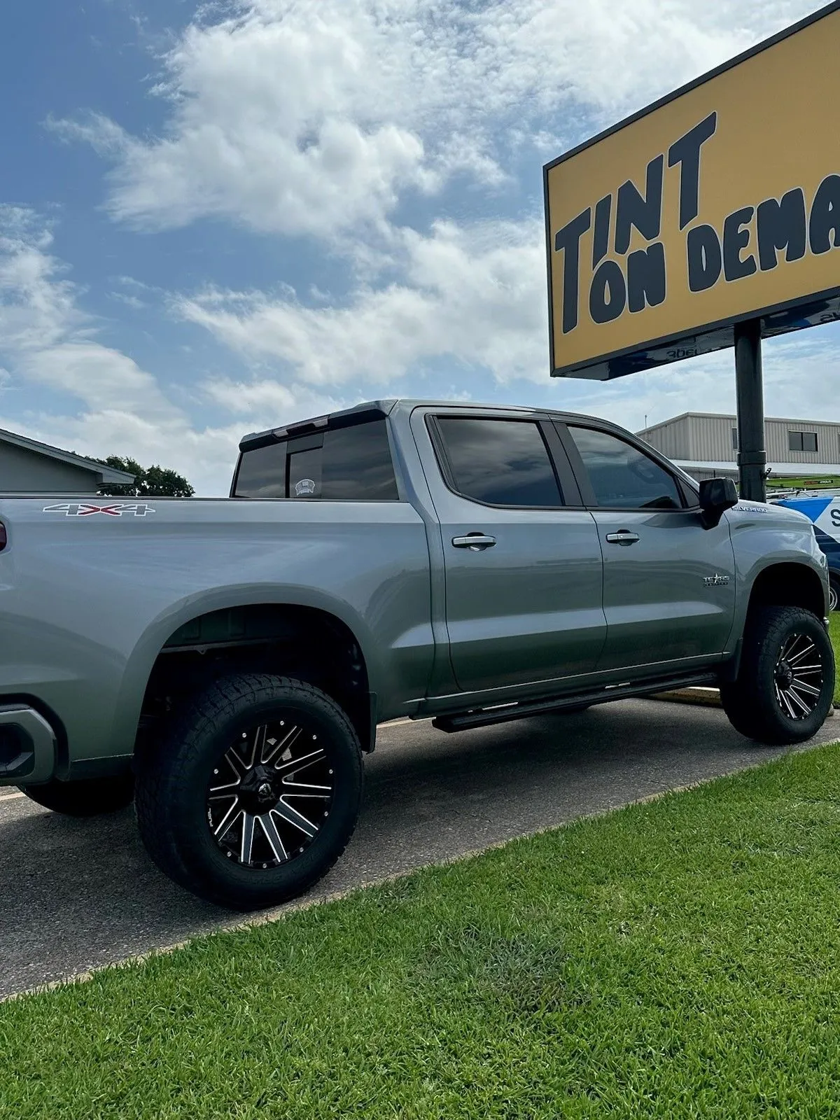 A silver truck is parked in front of a tint on demand sign.