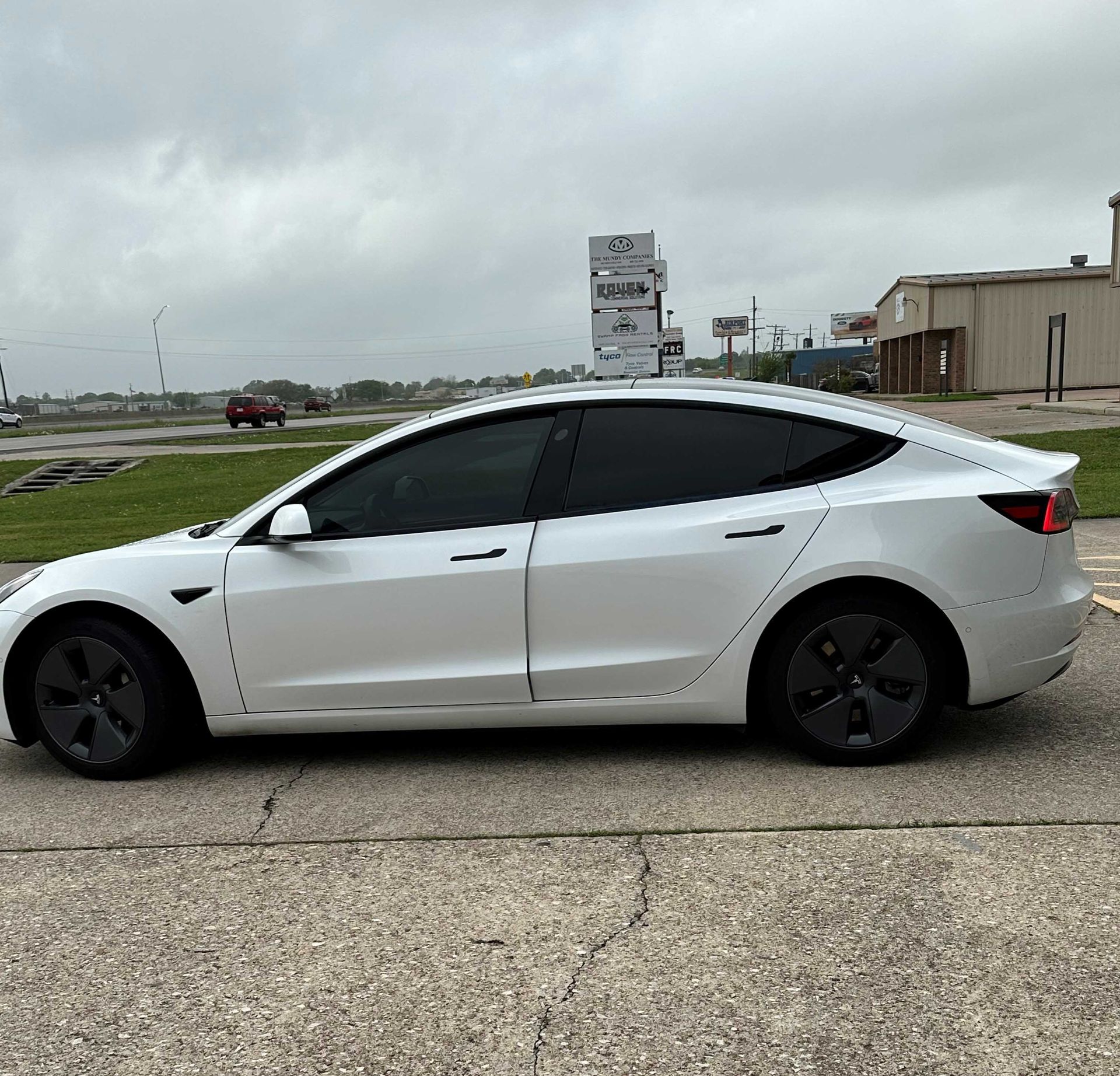 A white tesla model 3 is parked on the side of the road