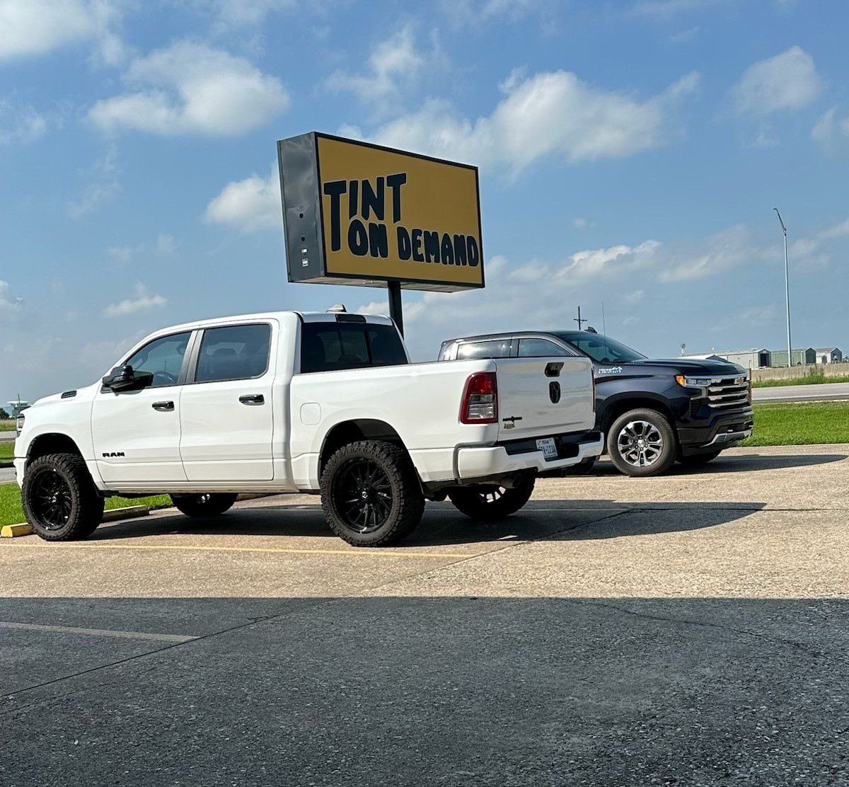 Two trucks are parked in front of a yellow sign that says tint tom delima.