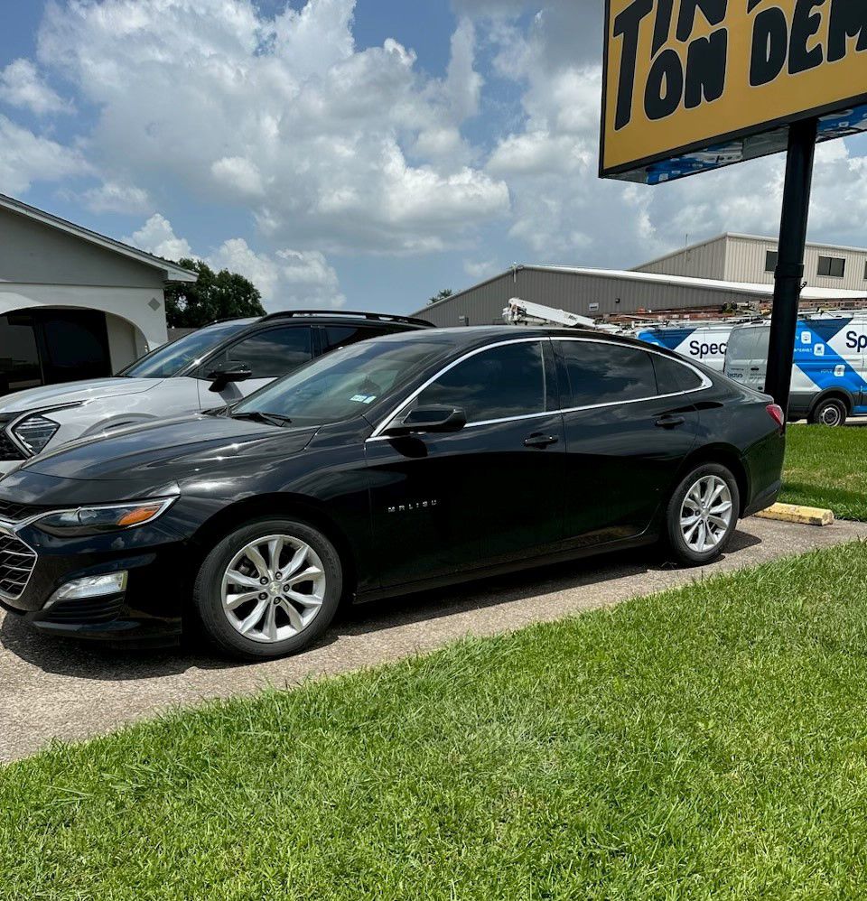 A black car is parked in front of a car dealership.