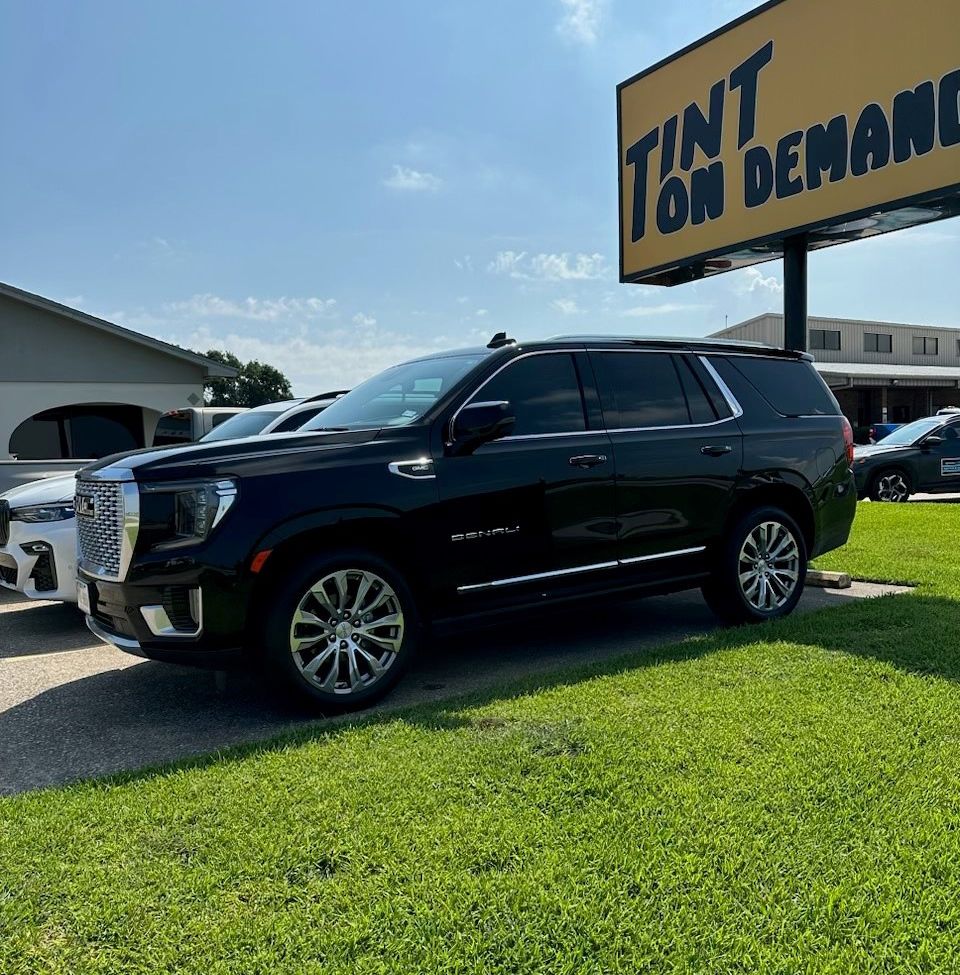 A black suv is parked in front of a billboard that says tint on demand.