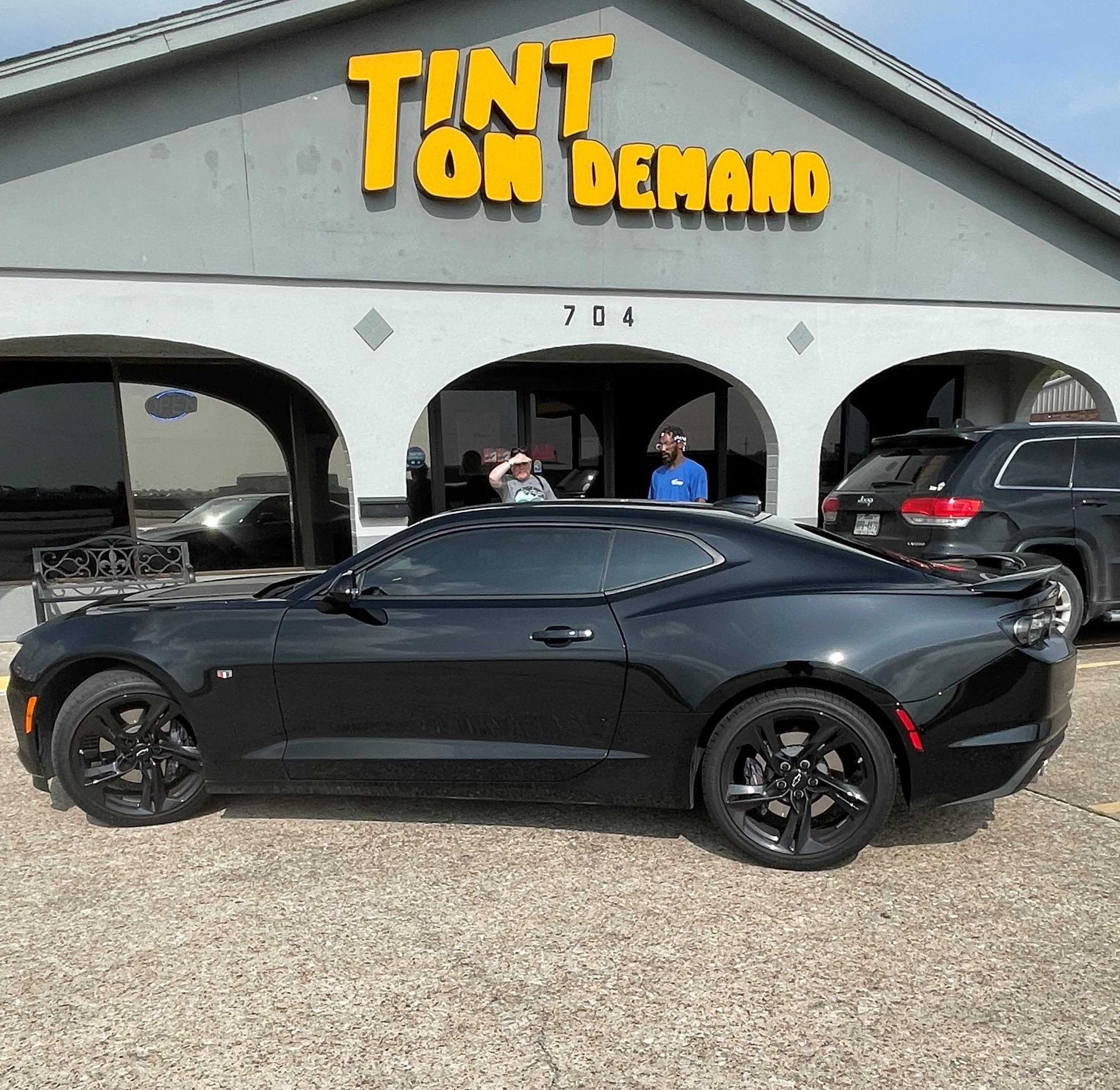 A black car is parked in front of a tint on demand store
