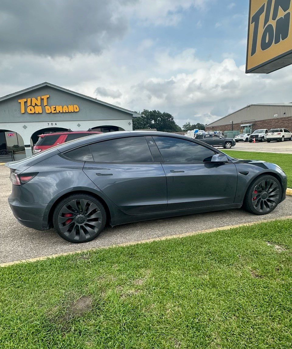 A tesla model 3 is parked in front of a tint shop.