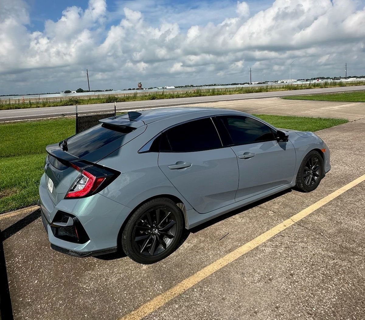 A gray honda civic hatchback is parked in a parking lot.