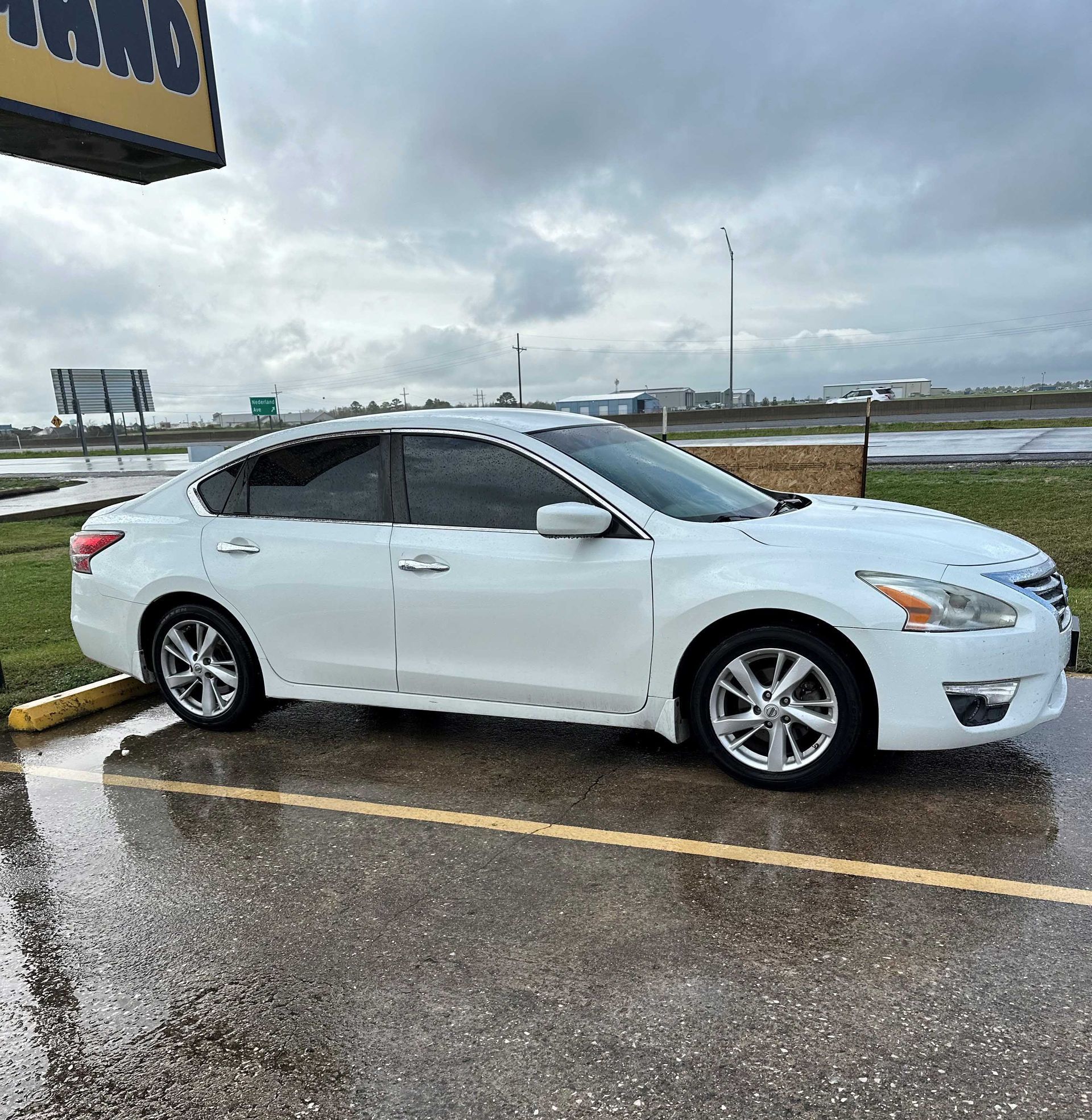 A white car is parked in a parking lot on a rainy day.