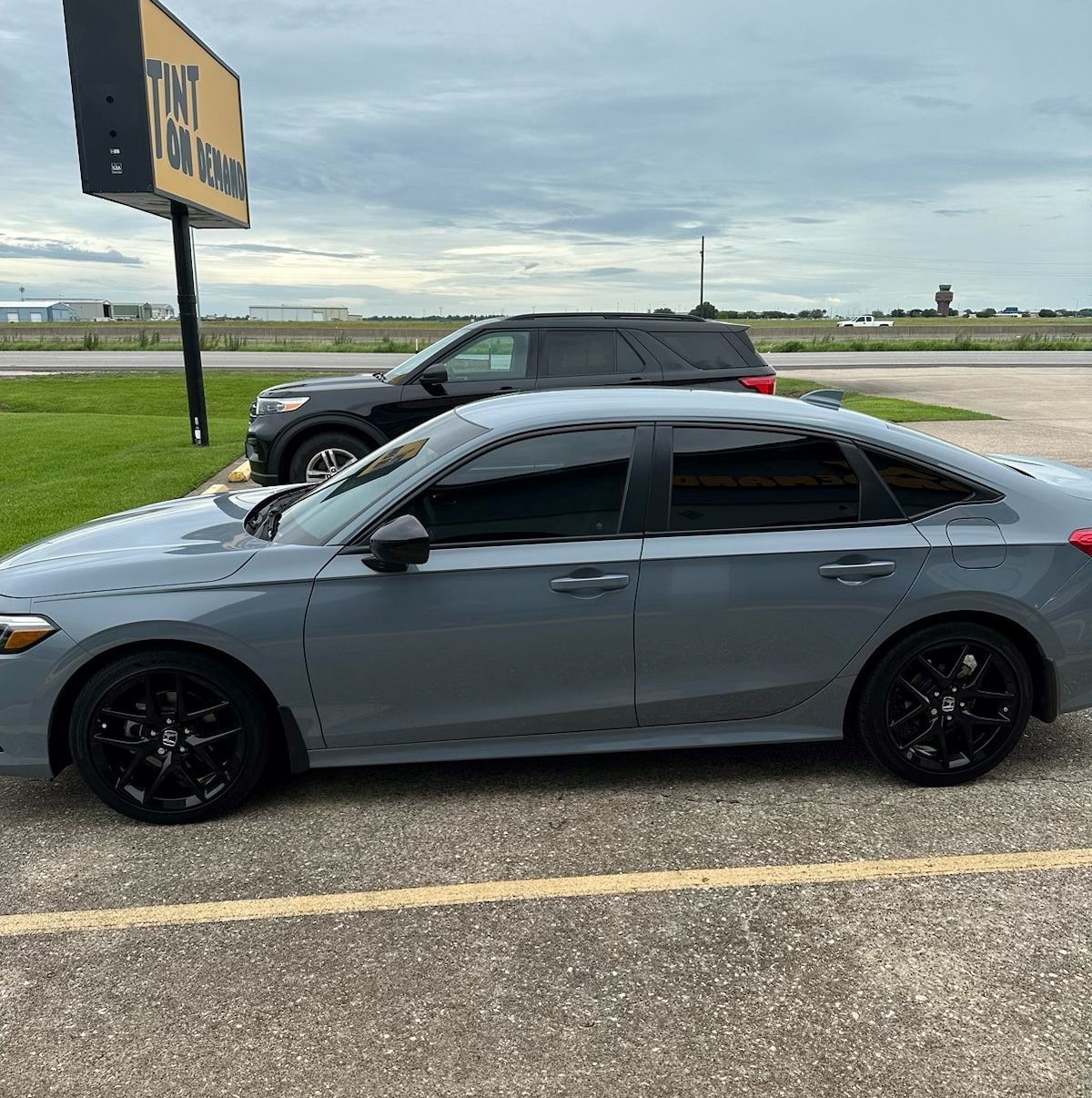 A gray car is parked in a parking lot next to a billboard that says taxi on it.