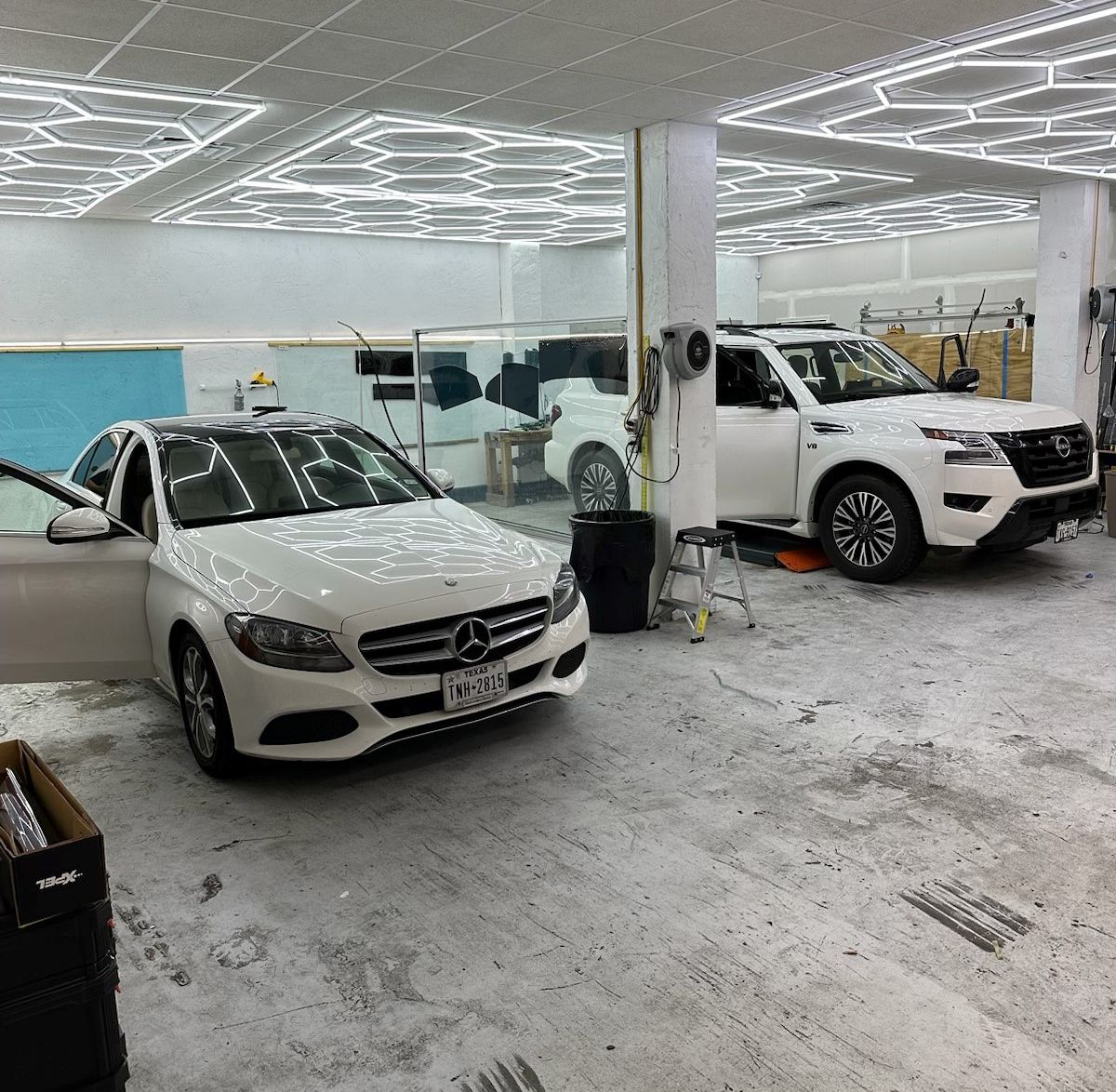 Two white cars are parked in a garage with their doors open.