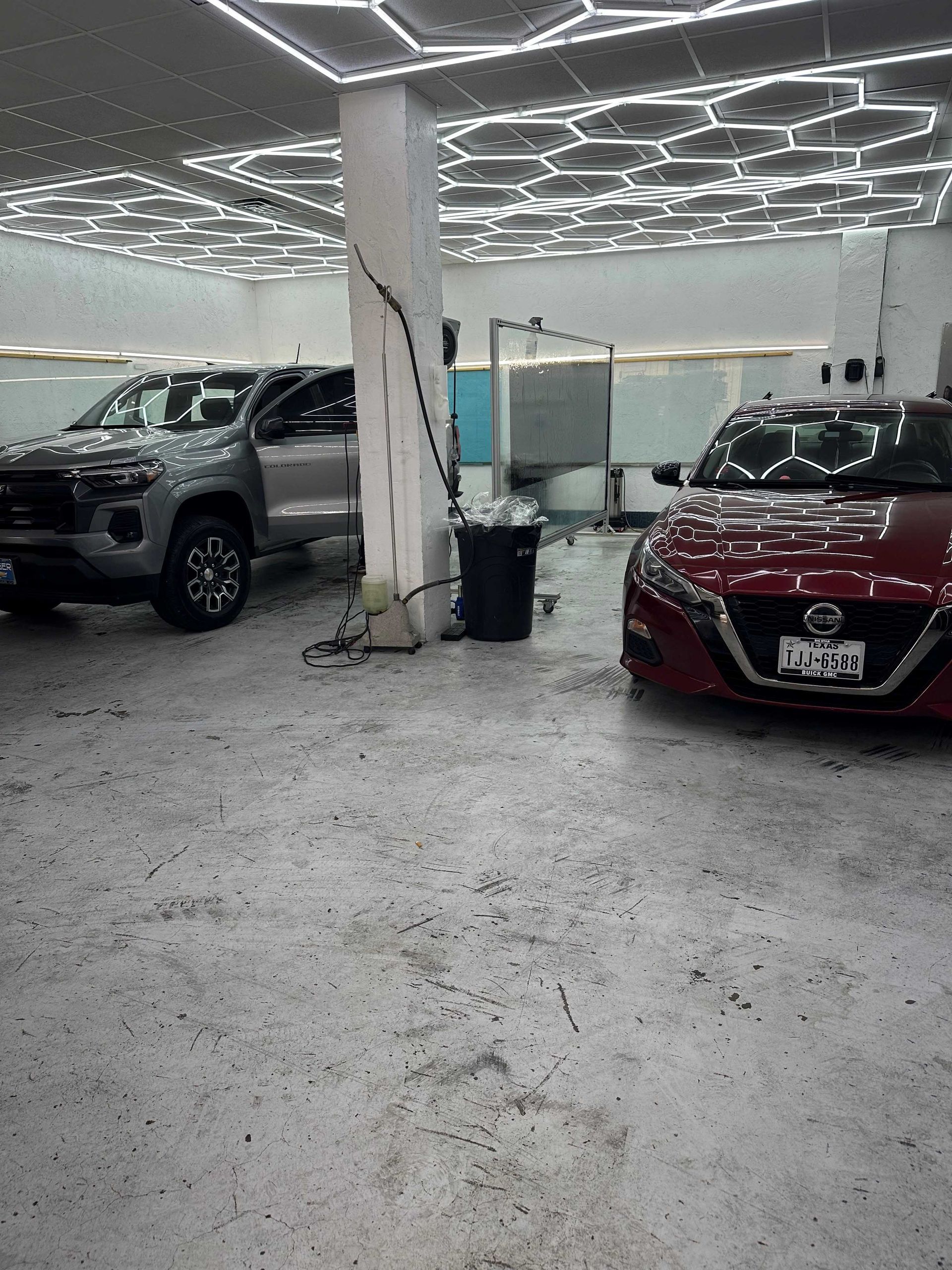 A red car is parked next to a silver truck in a garage.