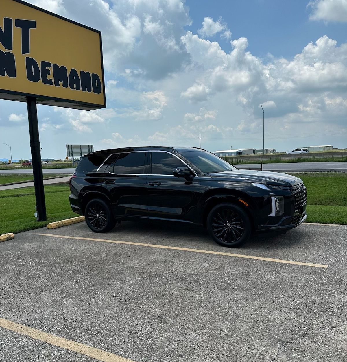 A black suv is parked in a parking lot under a sign that says no demand
