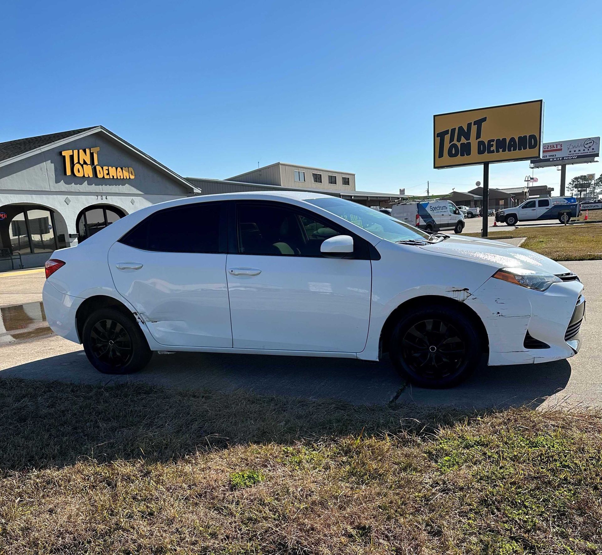 A white car is parked in front of a building that says tint on demand