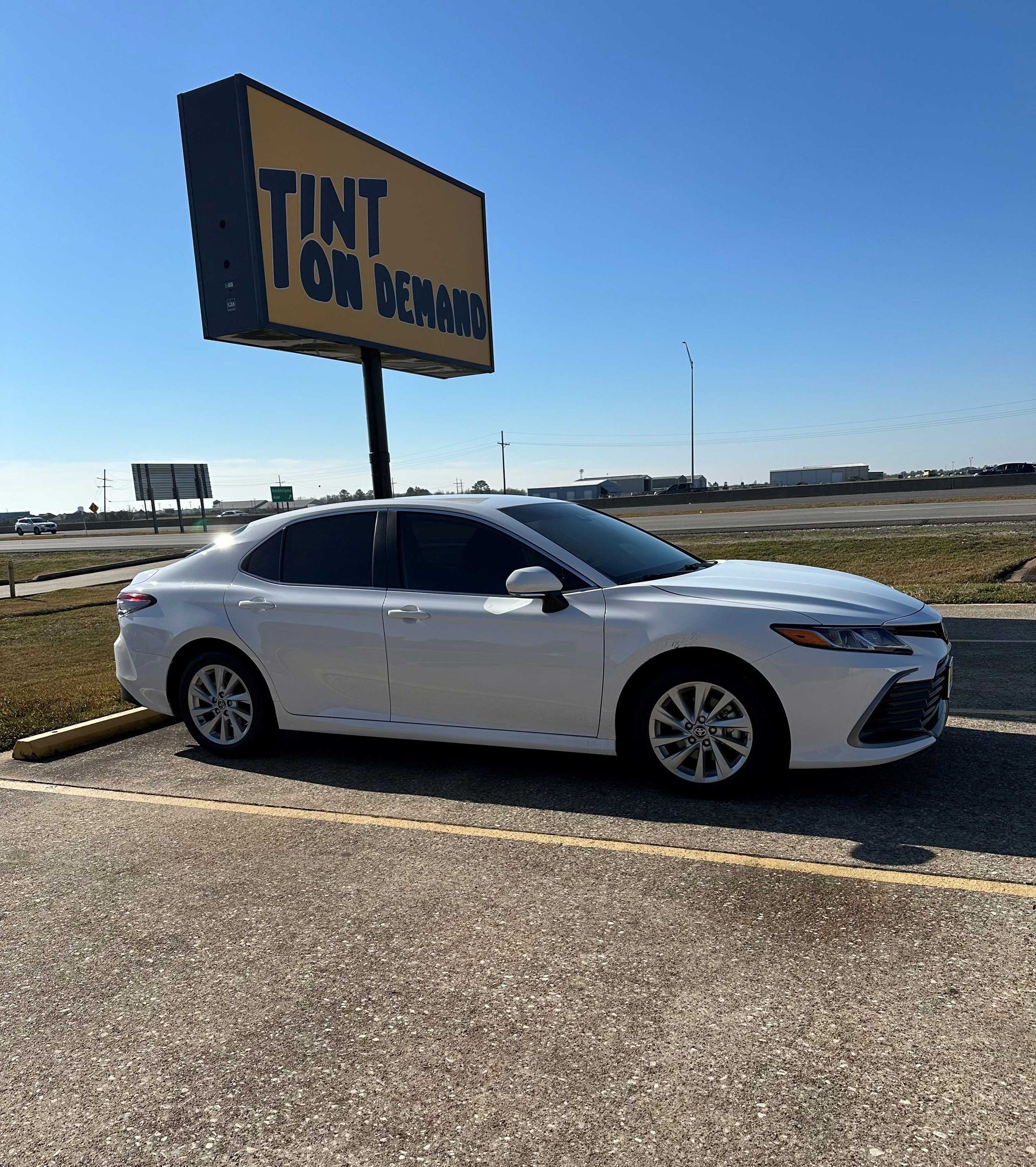 A white car is parked in front of a tint on demand sign.