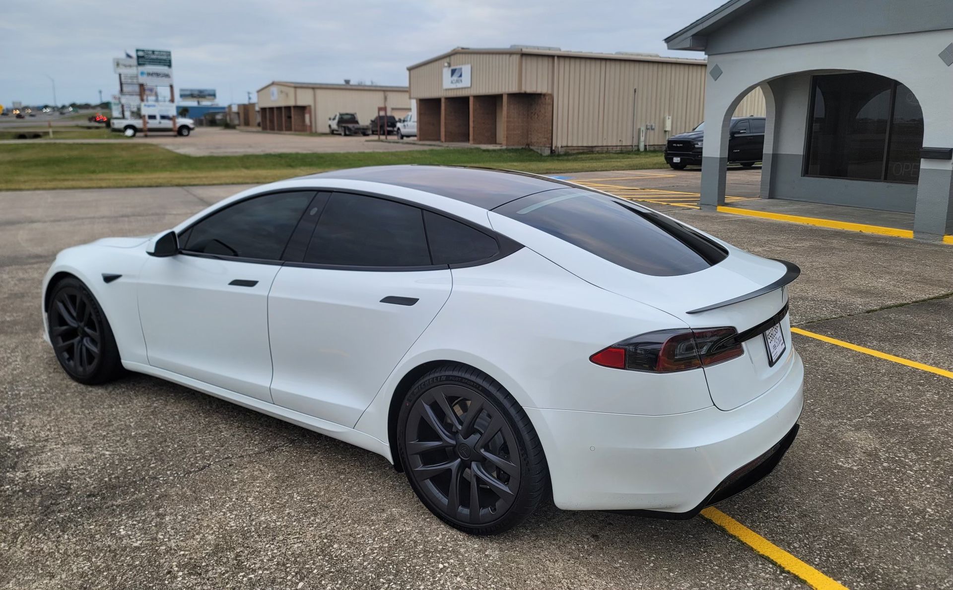 A white tesla model s is parked in a parking lot in front of a building.