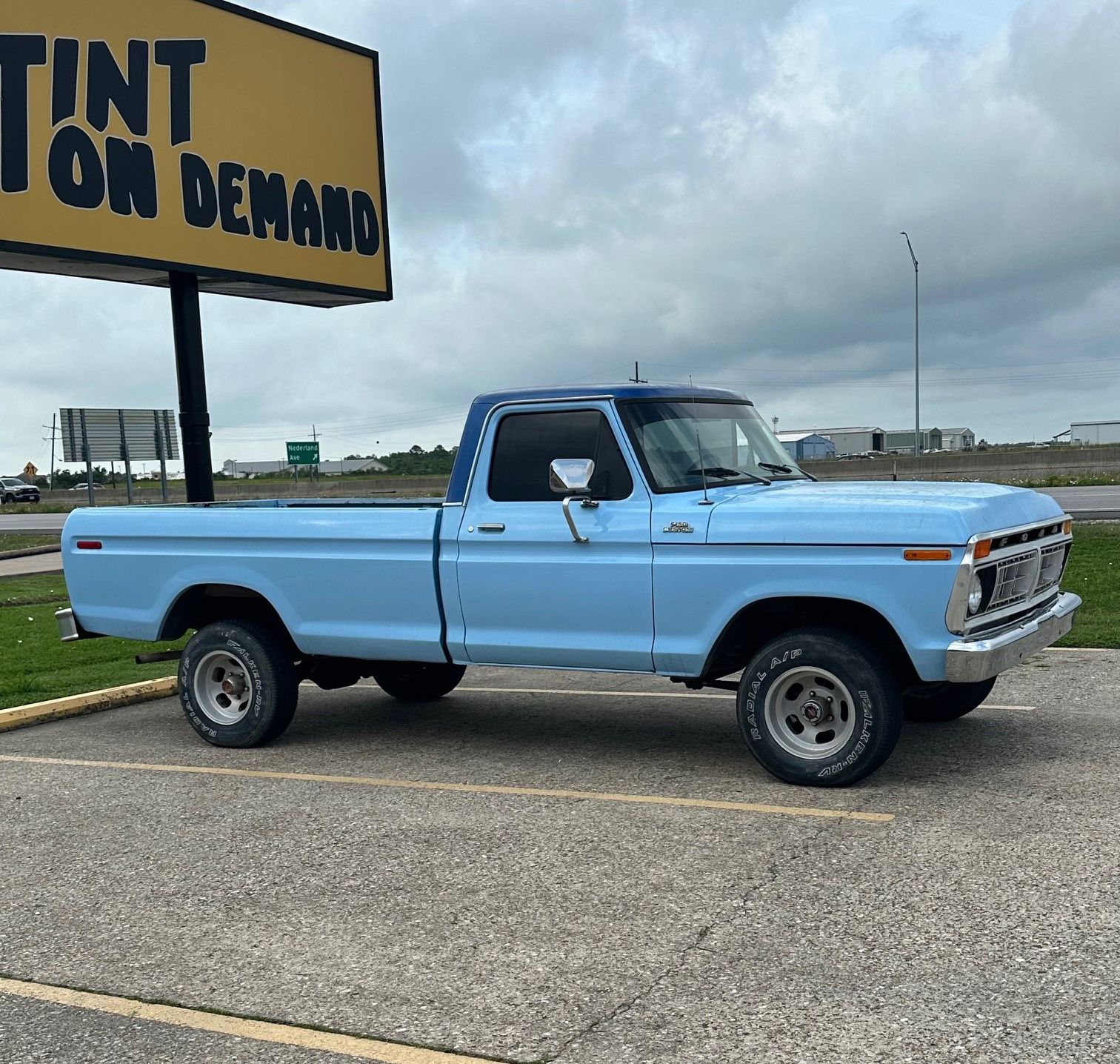 A blue truck is parked in front of a tint on demand sign