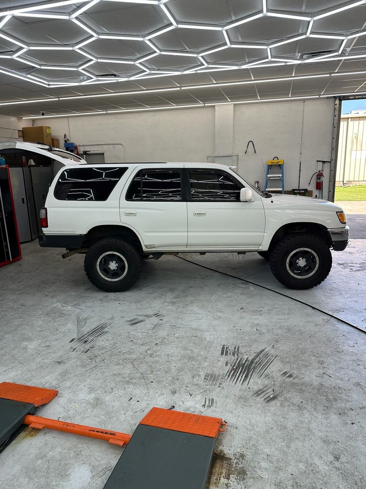 A white suv is parked in a garage next to a lift.