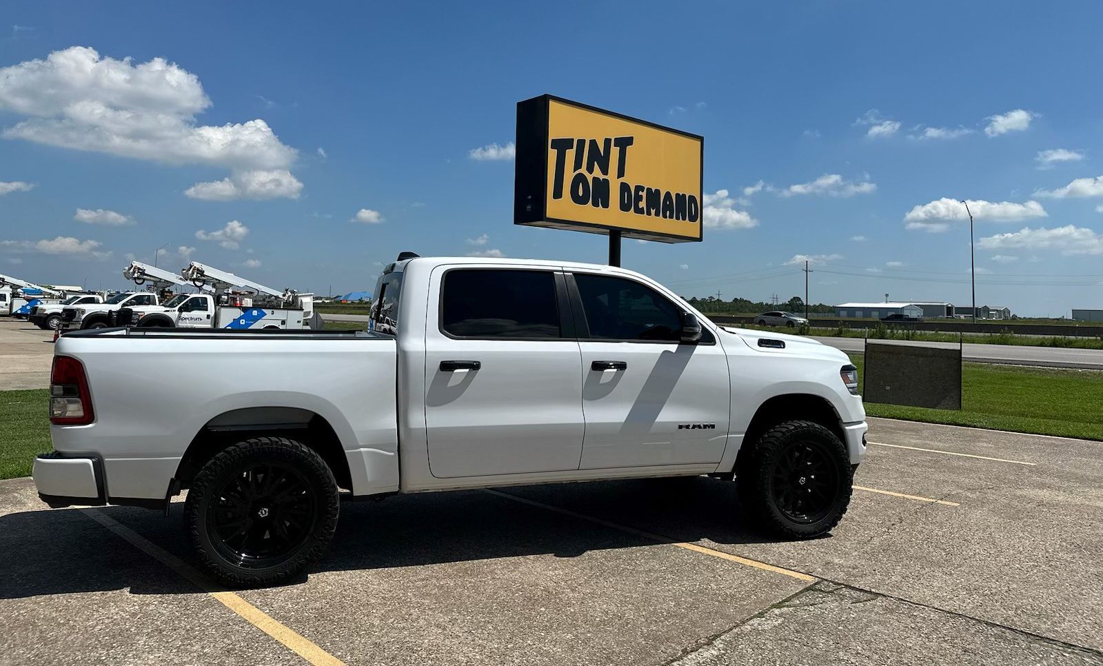 A white truck is parked in a parking lot under a yellow sign that says tint on windows.