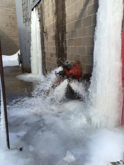 Fire hydrant spewing water and ice on brick wall, creating large ice formations.