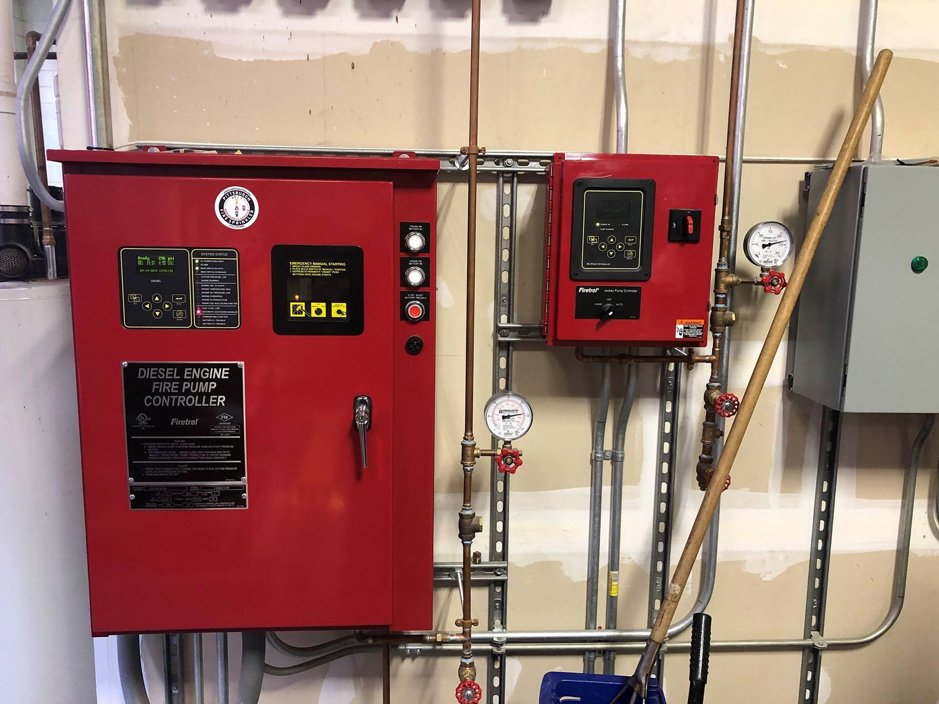 Red water pump control panel with gauges and pipes against a wall.