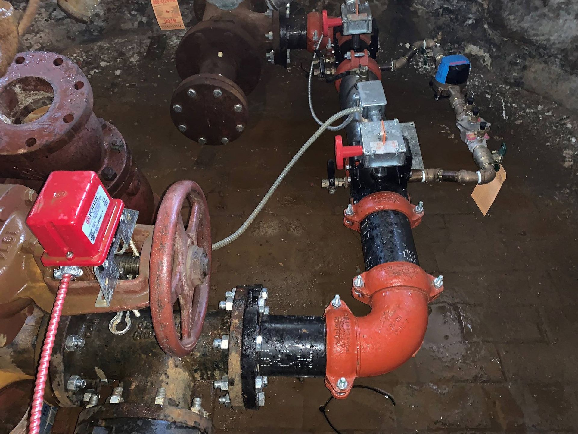 Water pipes and valves in a ditch. Red and black pipes, valves with electronic controls, industrial setting.