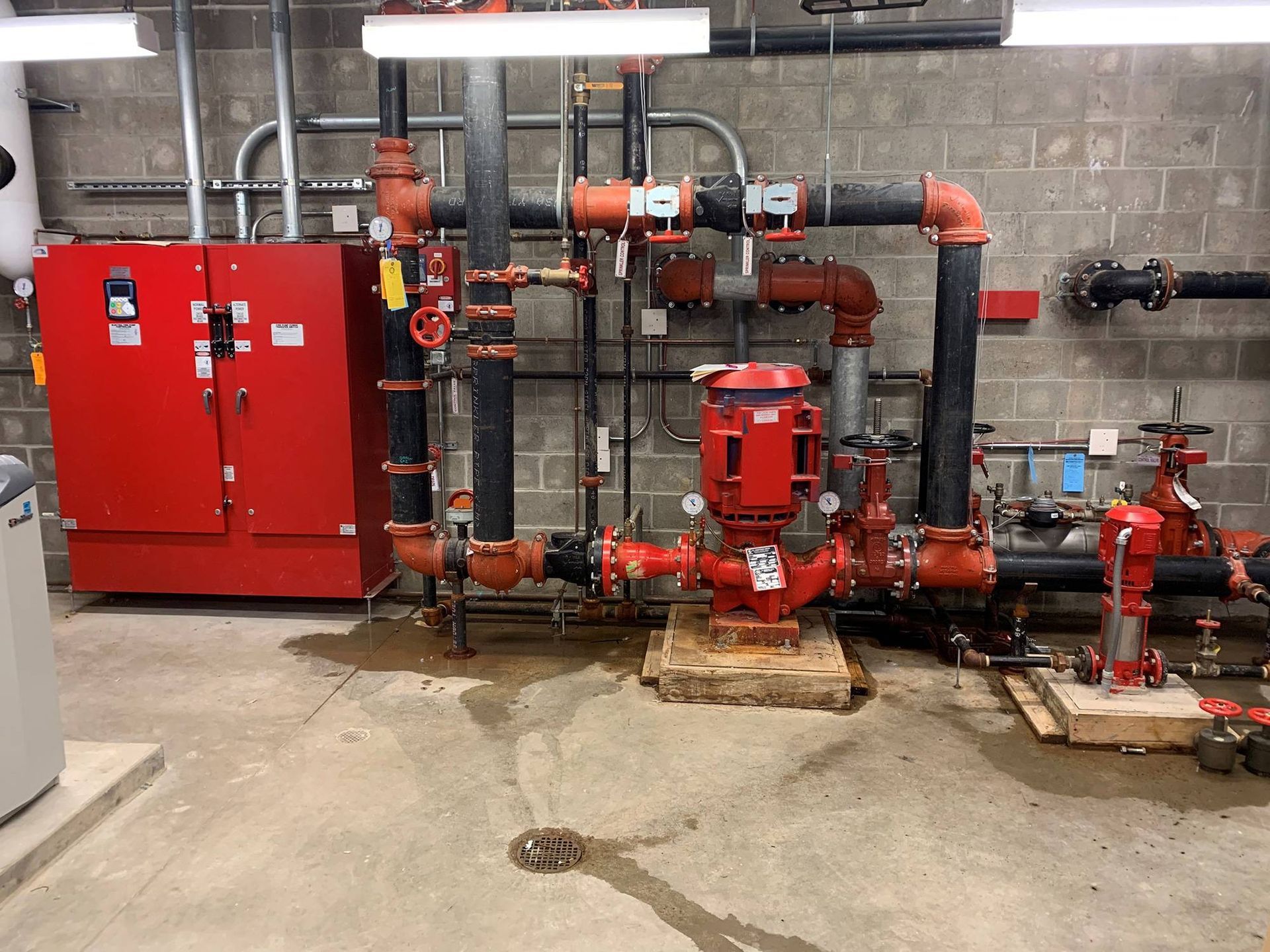 Red fire pump system in a utility room with piping, control panel, and concrete floor.
