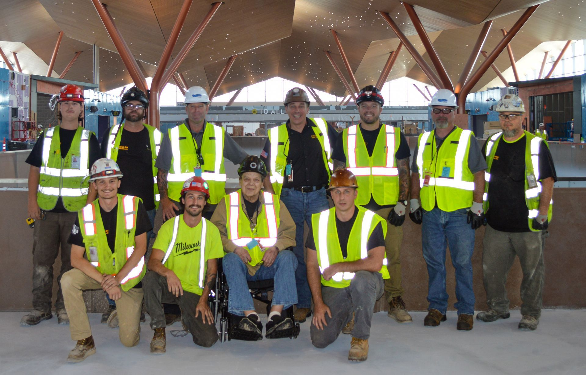 Construction workers in safety vests and hard hats pose for a group photo under a modern ceiling.