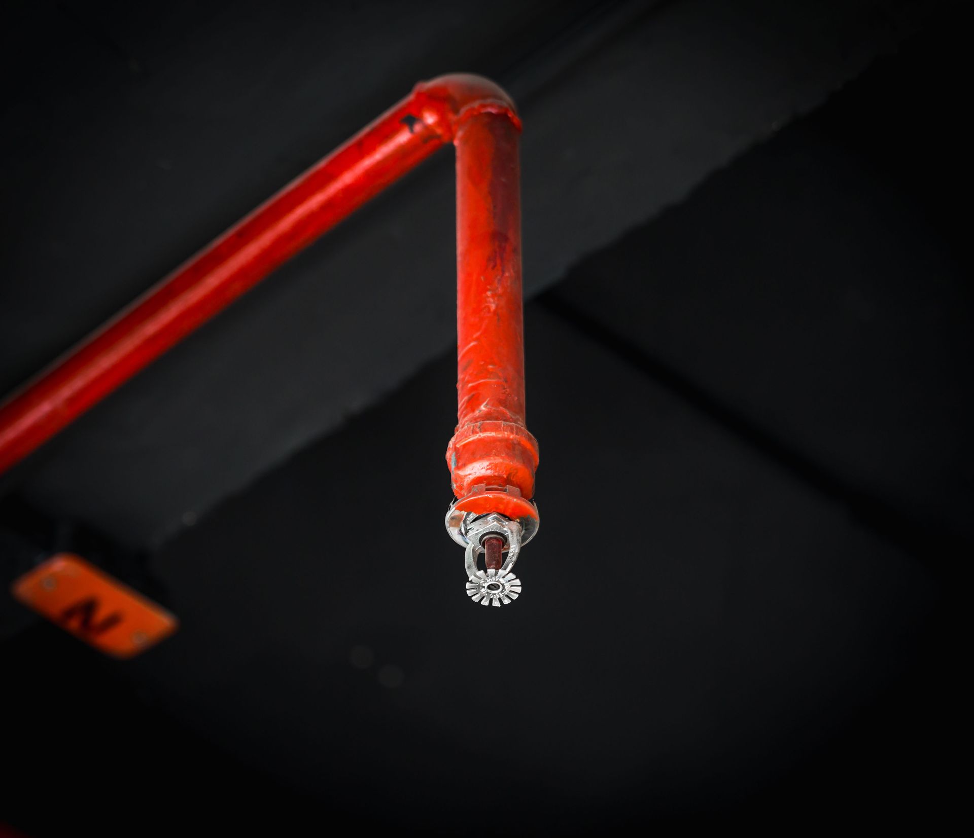 Close-up of a red fire sprinkler pipe with a small water droplet hanging from the nozzle