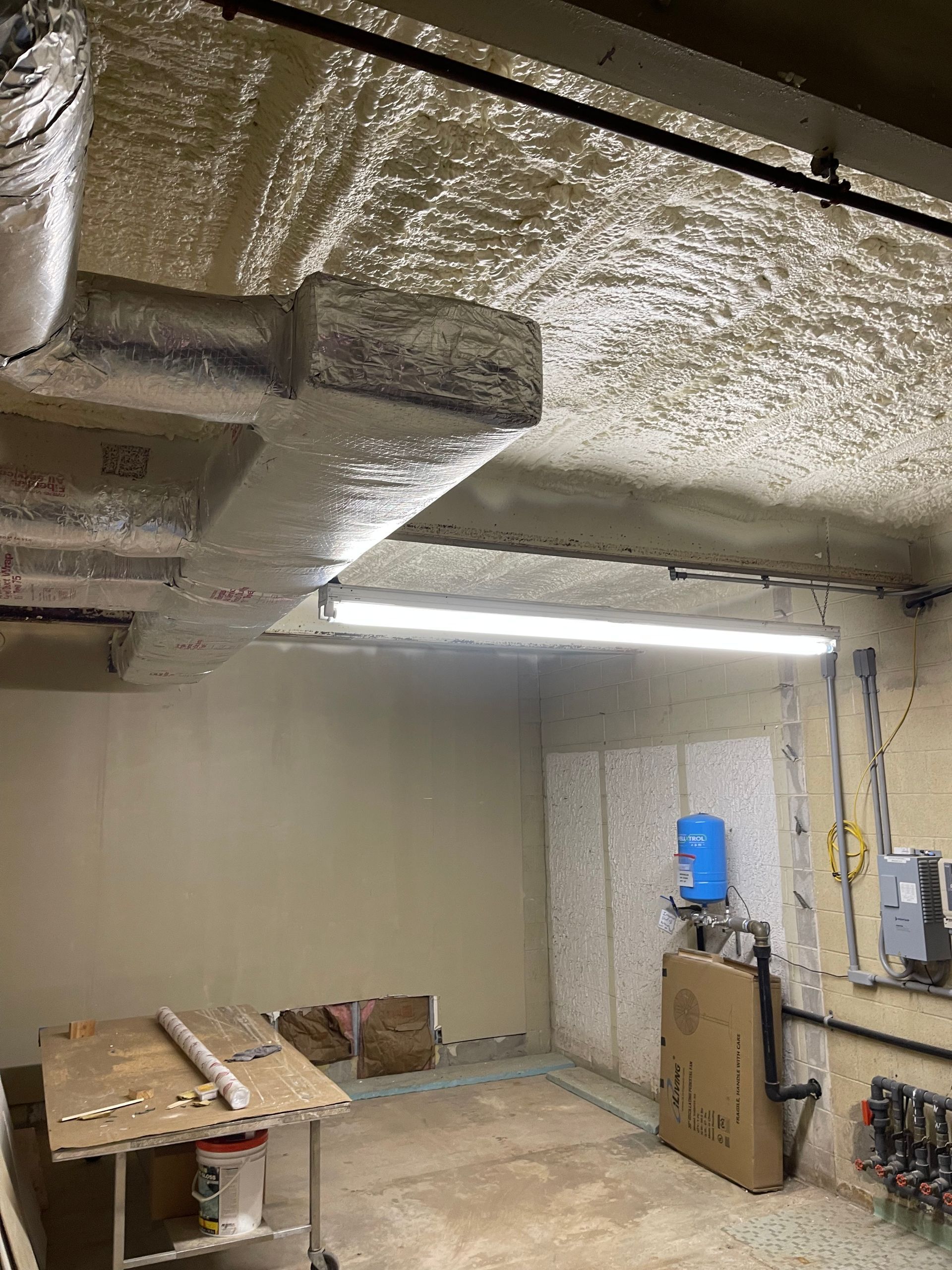 Basement interior with exposed ducts and piping, beige walls, and a blue pressure tank.