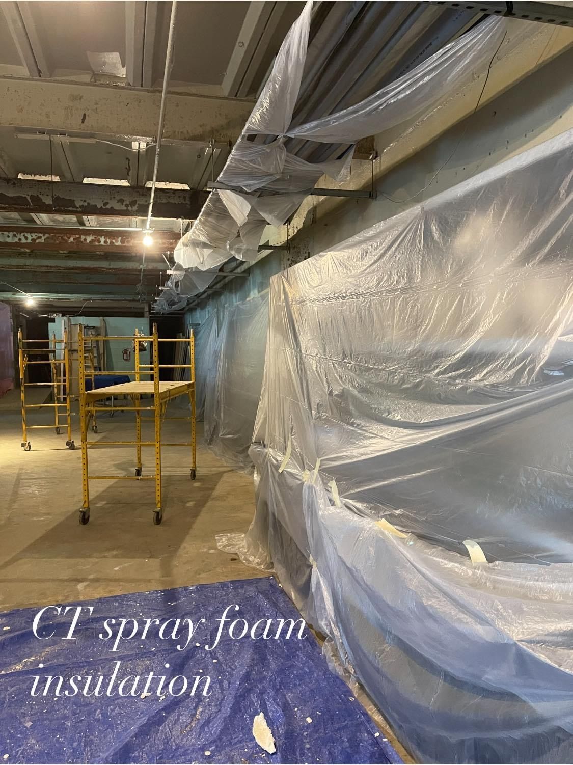 Construction site with plastic sheeting, scaffolding, and spray foam insulation.