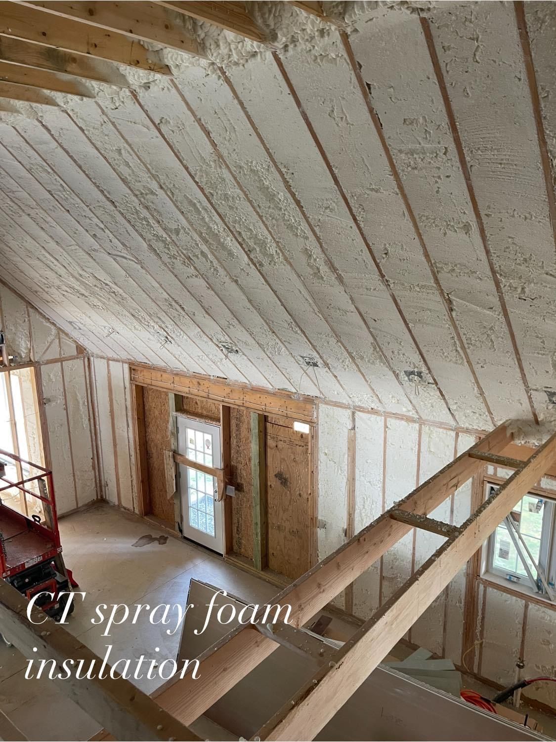 Interior view of a building with spray foam insulation on the walls and ceiling. Wooden beams are visible.