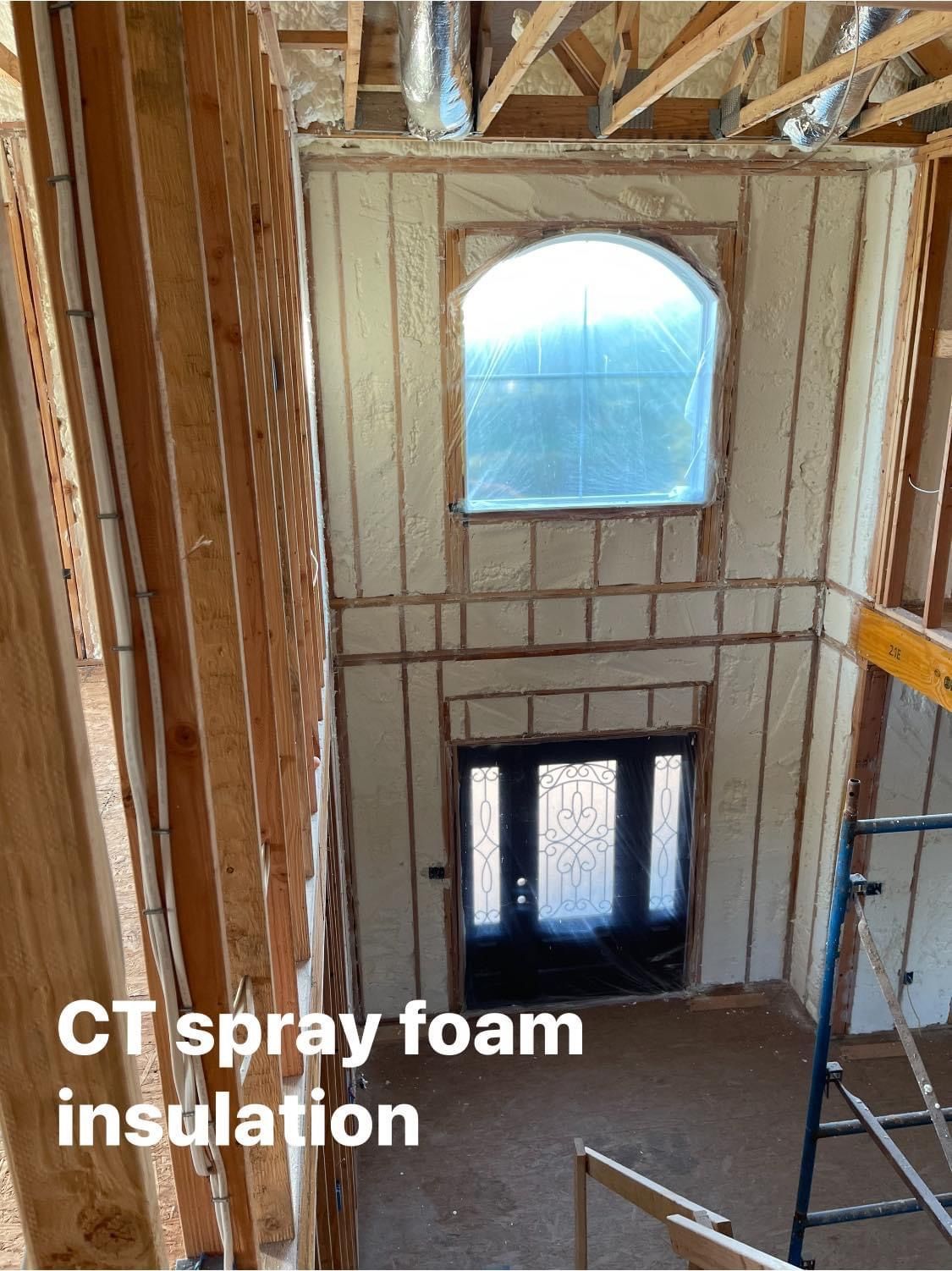Interior view of a building with spray foam insulation. A large arched window and front door are visible.