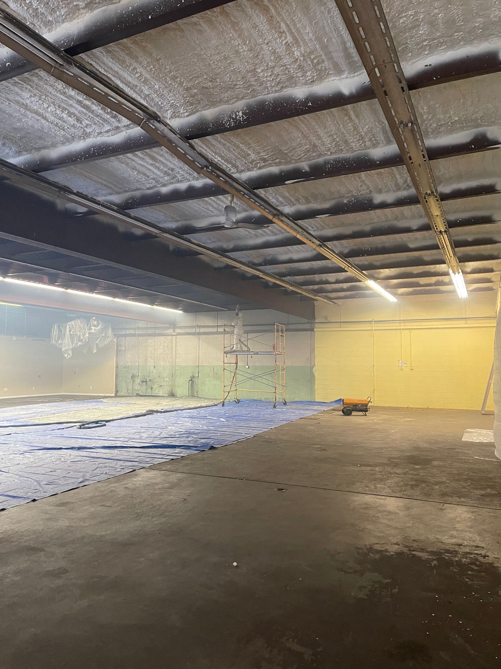 Interior of a building with a wet floor, ceiling beams, and a basketball hoop. Blue material on the floor.