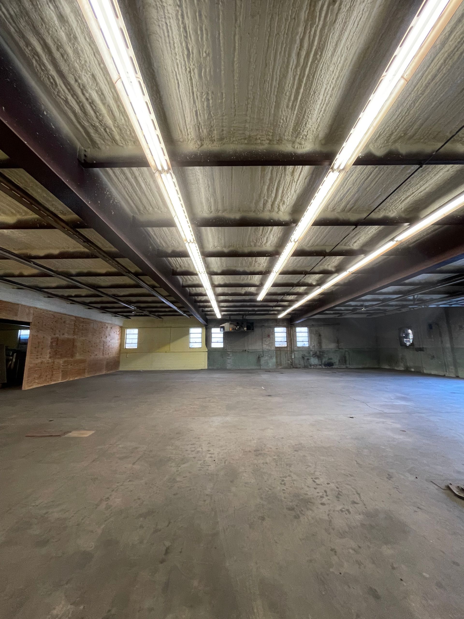 Empty warehouse interior with concrete floor, metal beams, and fluorescent lights.