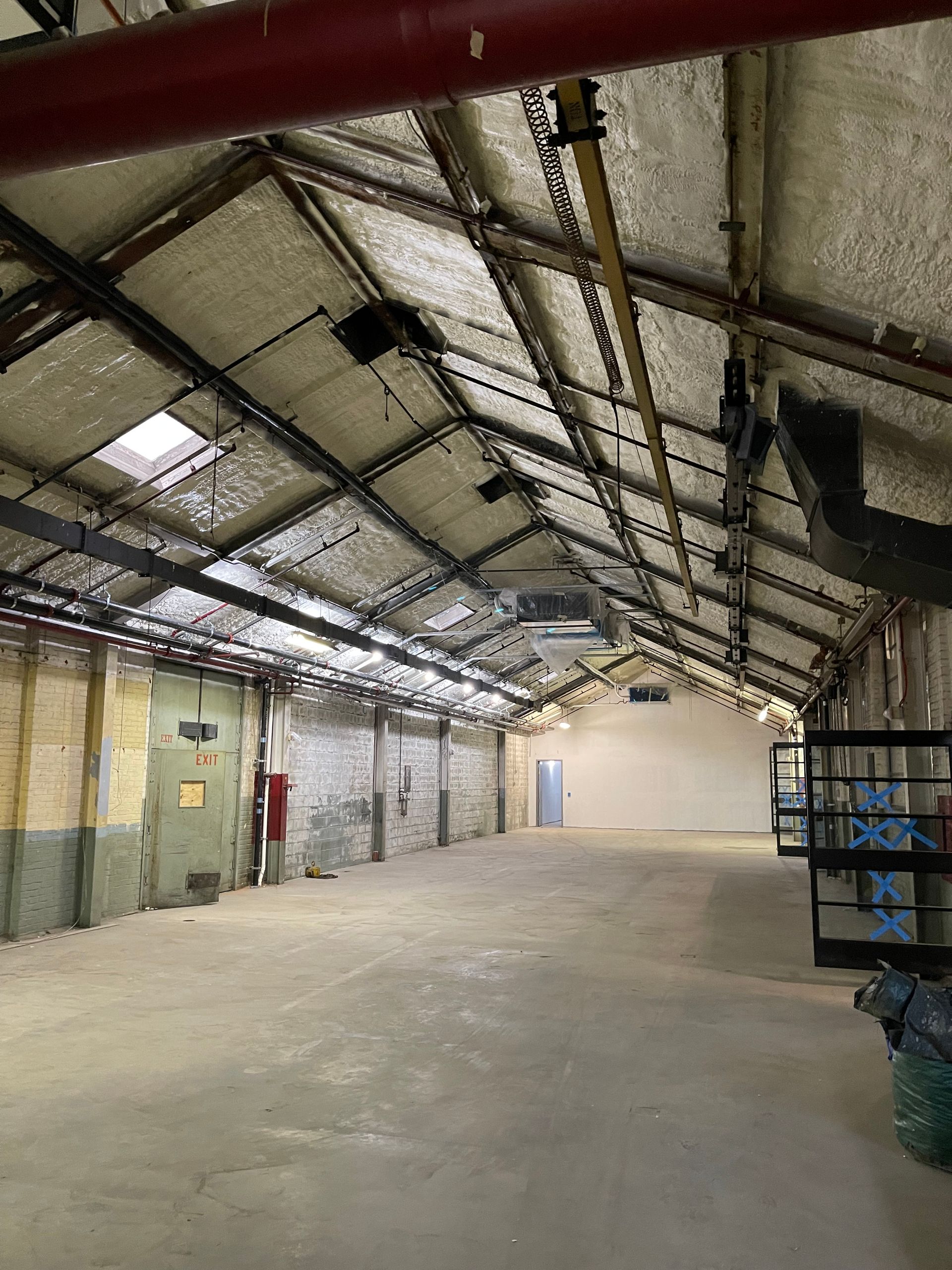 Empty warehouse interior with high, sloped ceiling. Concrete floor, brick walls, and dim natural light.
