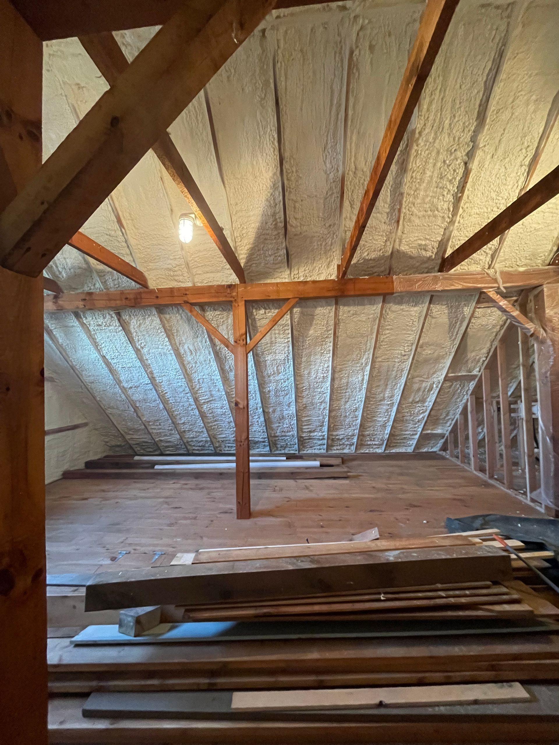 Interior view of an attic with spray foam insulation on the rafters and exposed wooden beams.