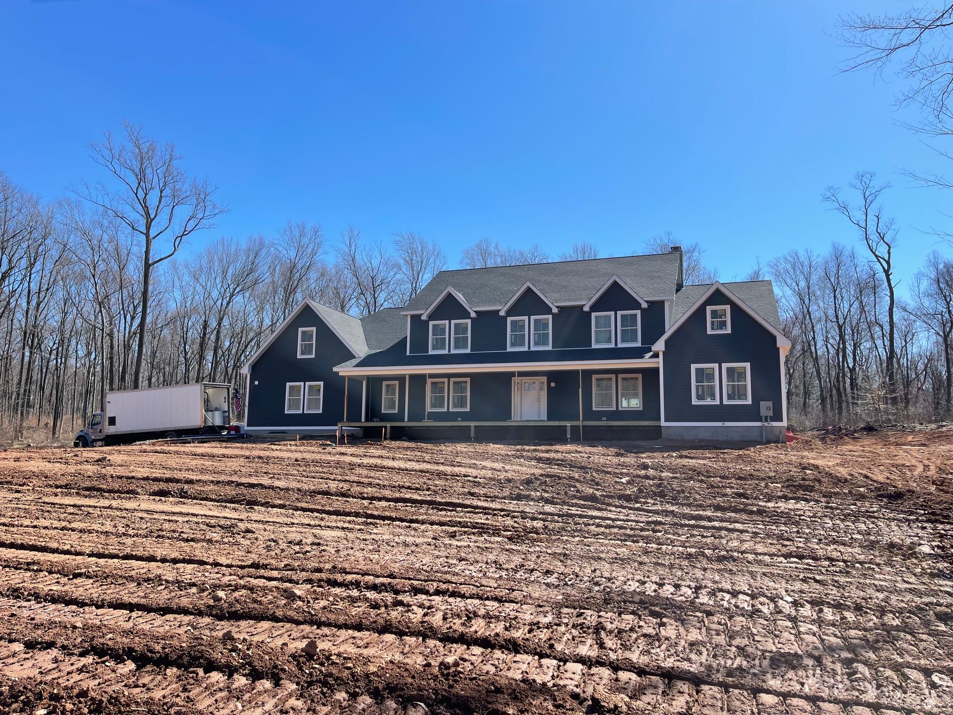 Blue house under construction, sitting on cleared land, with trees in the background. Clear, blue sky overhead.