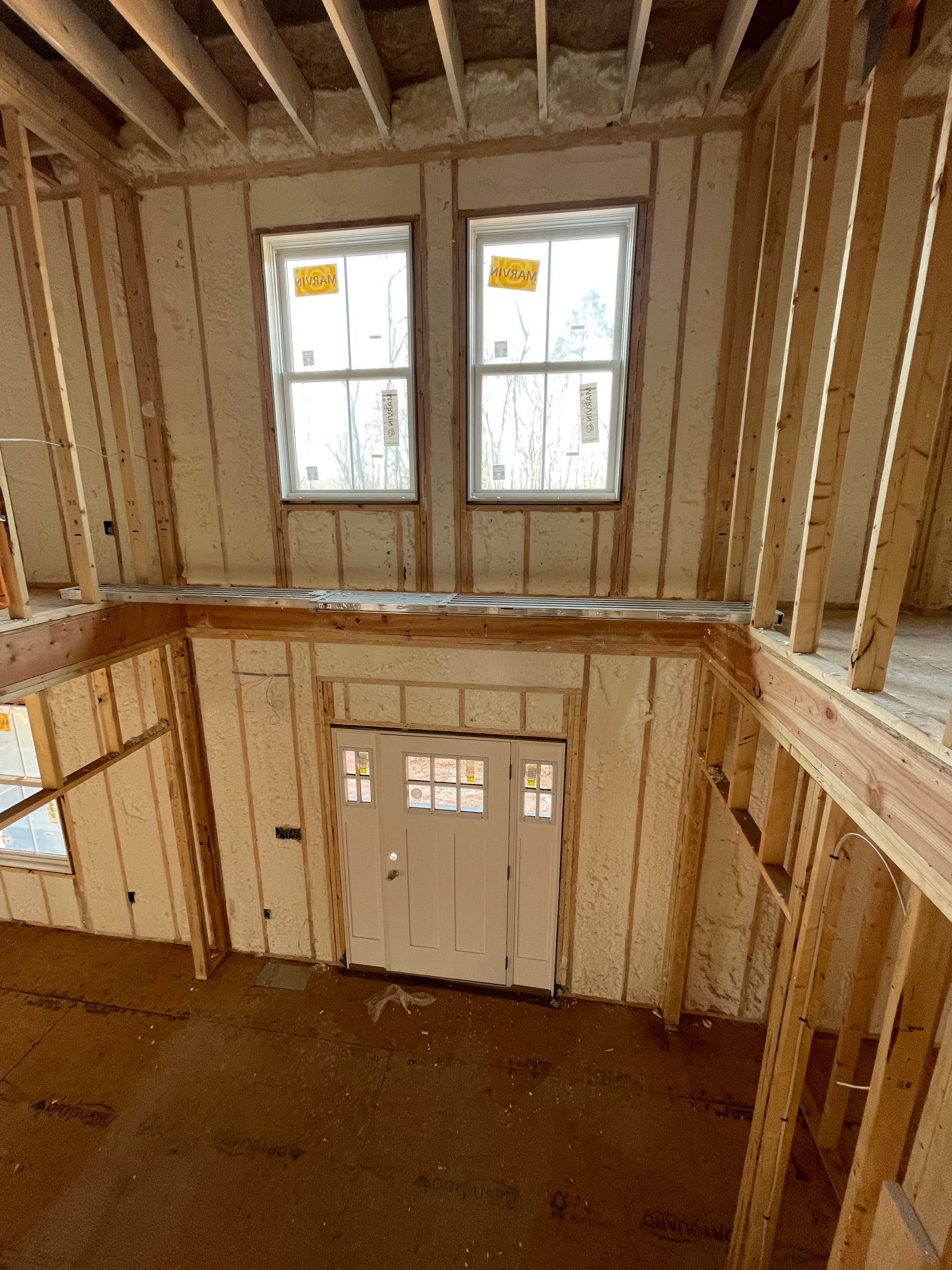 Interior view of a building under construction, showing a door, windows, and exposed wooden framing.