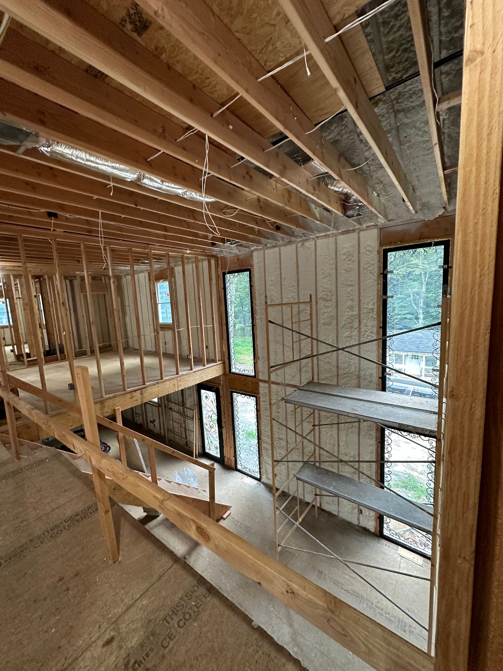 Interior view of a building under construction, showing exposed wooden framing, insulation, and windows.