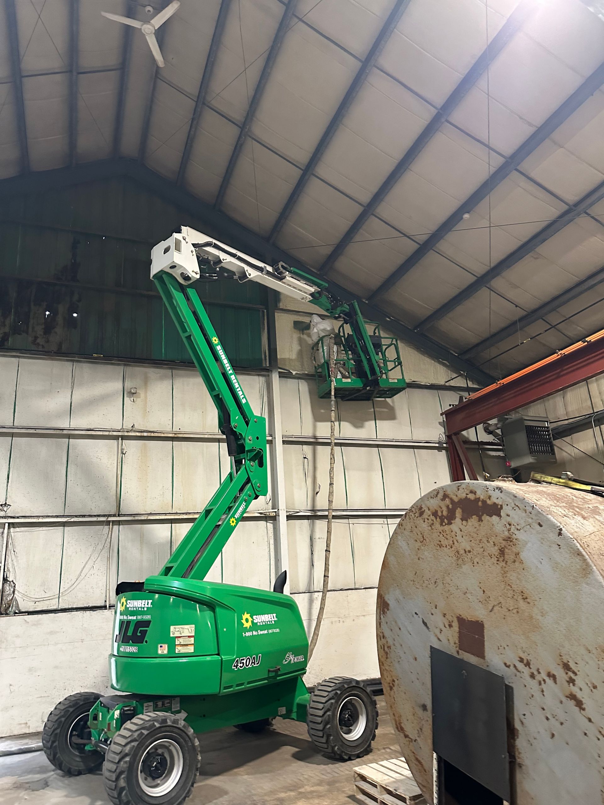 A green boom lift reaching toward a wall inside a warehouse.