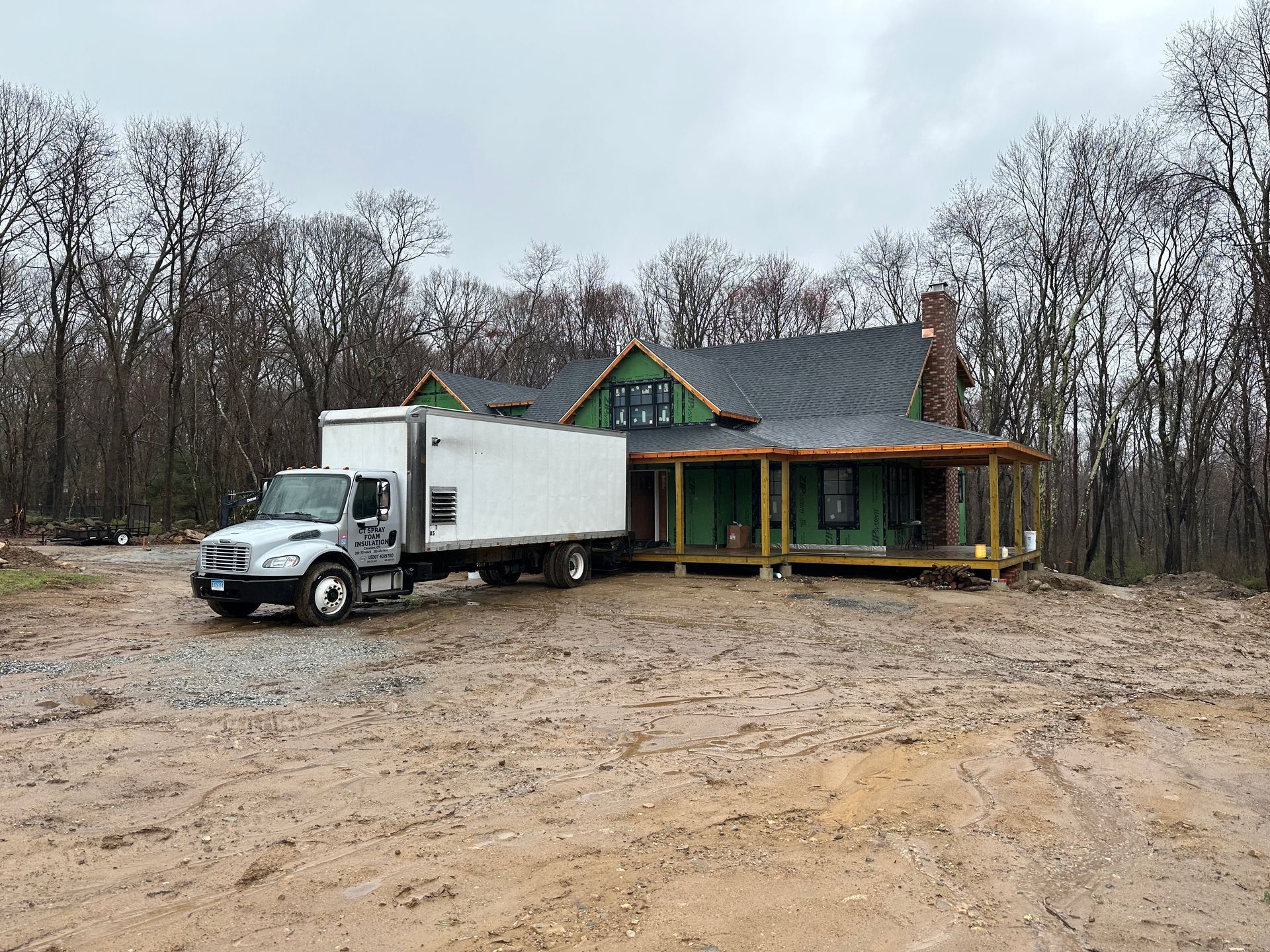 Truck parked in muddy yard near a partially constructed house with a porch and green trim.