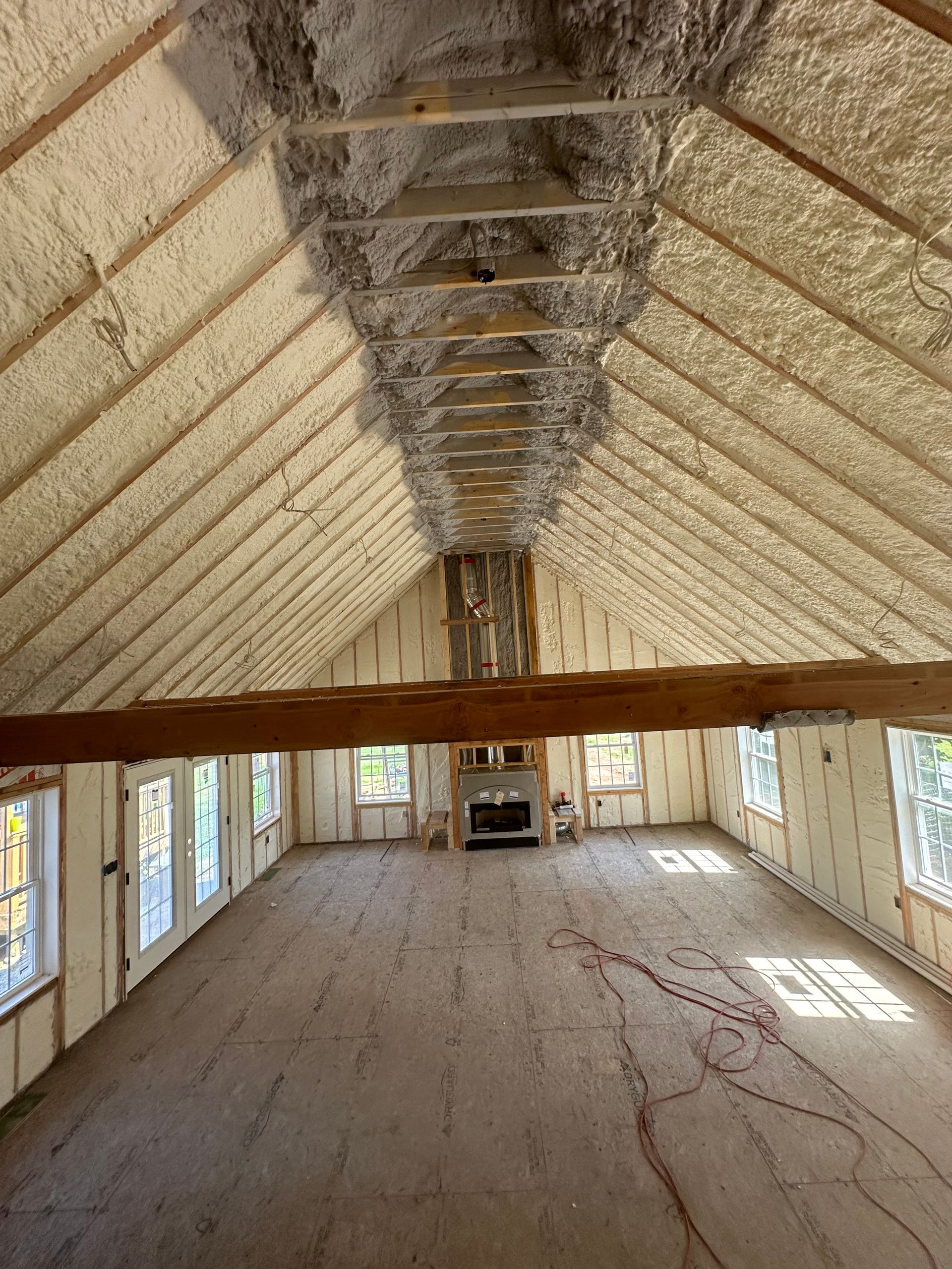 Interior view of an attic with spray foam insulation. A fireplace is centered with windows flanking the room.