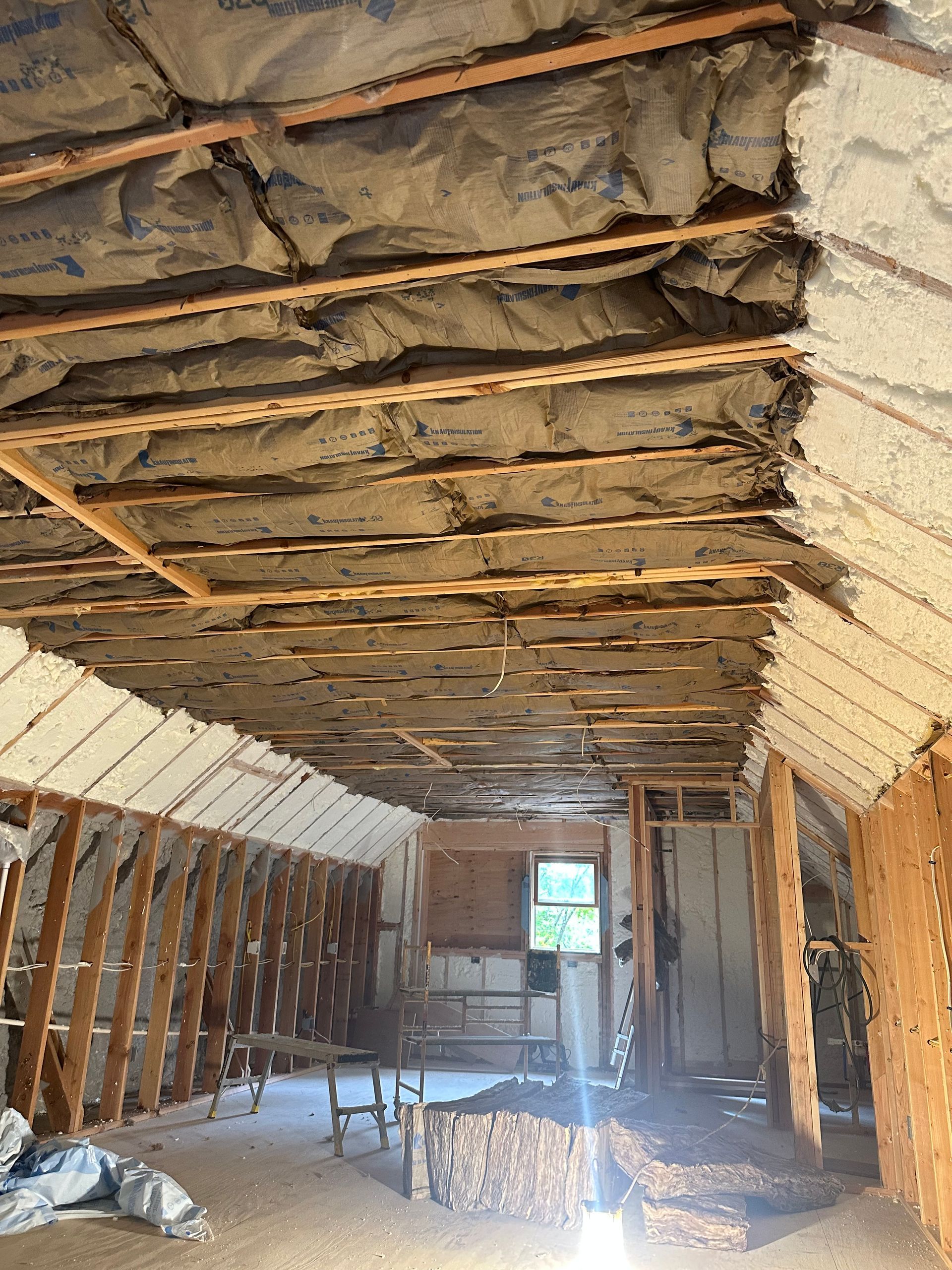 Interior of a room under construction with exposed wooden beams, insulation, and spray foam.